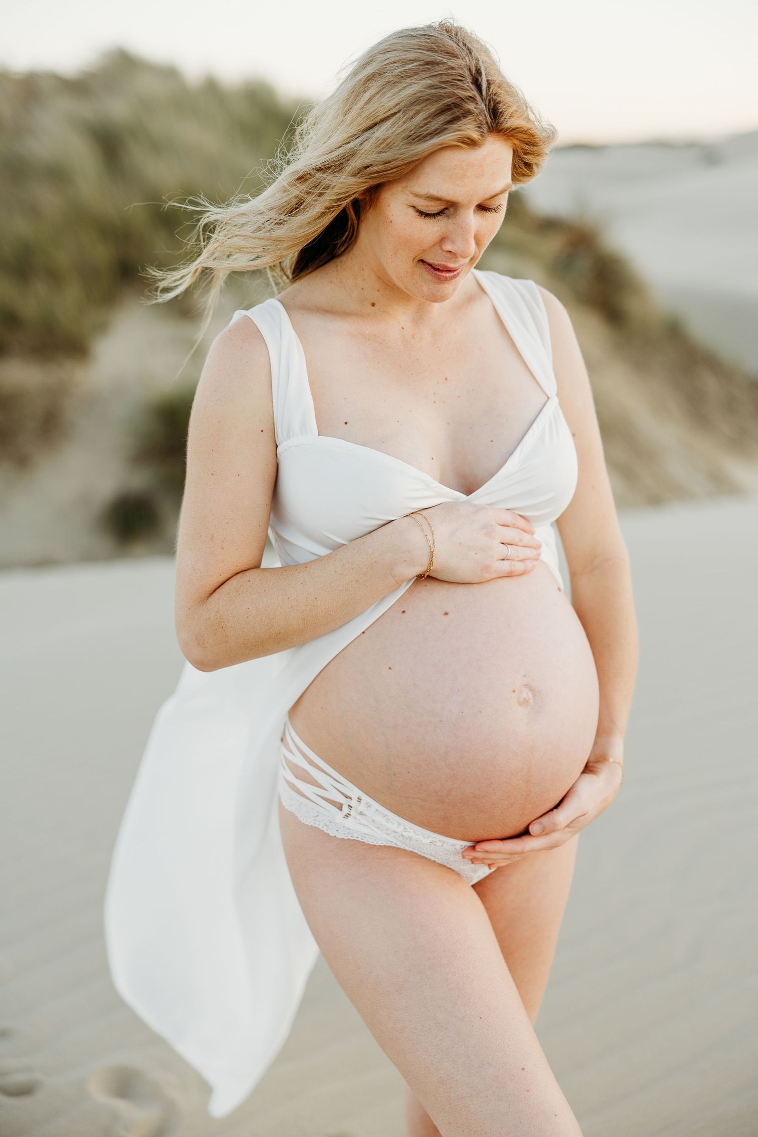 Maternity portrait on beach showing expecting mother in white swimwear.