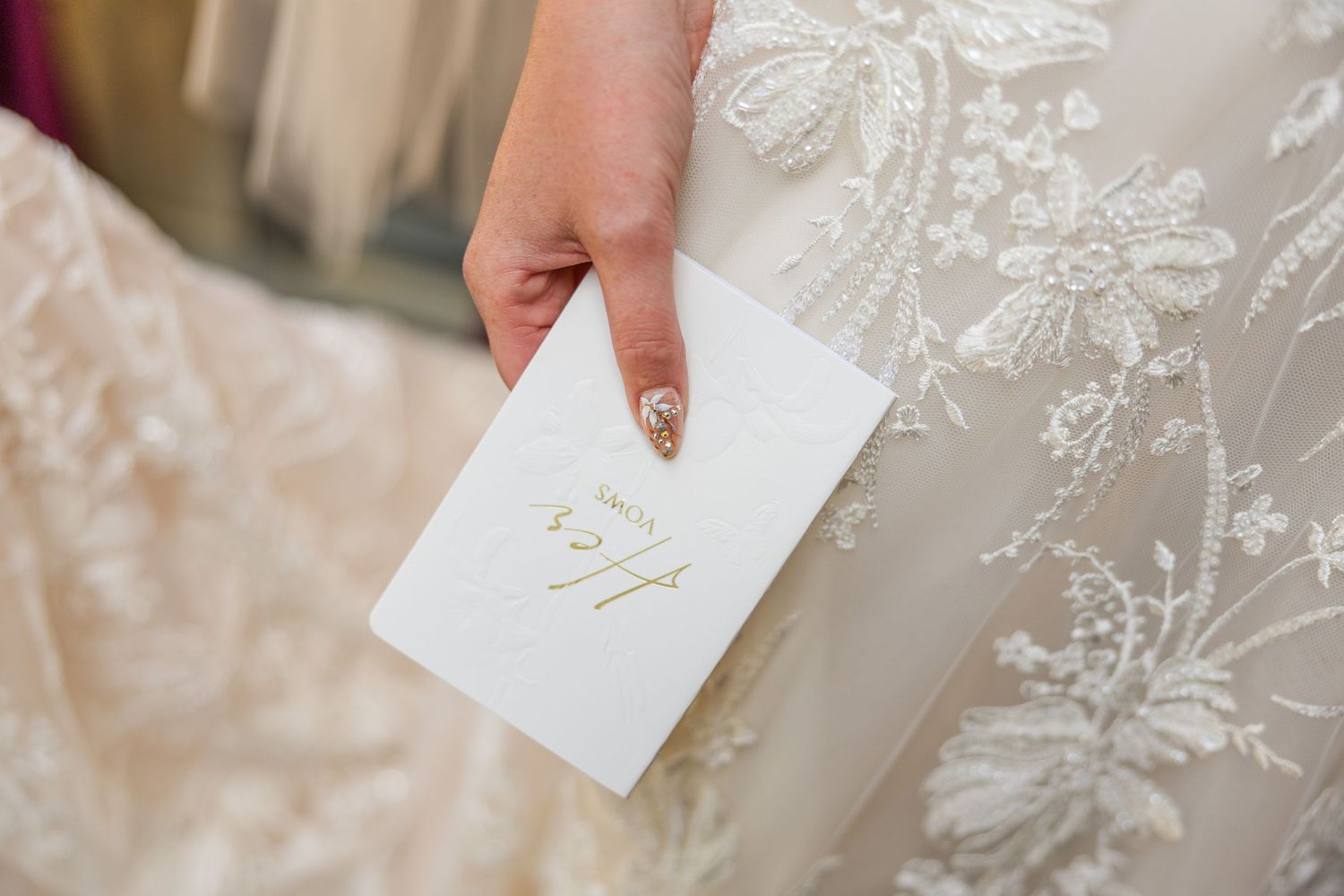 Close-up detail shot of a lace wedding dress and hand holding an elegant white note card.