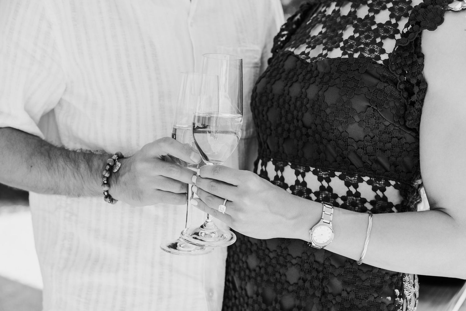 Black and white photo of couple holding champagne glasses together.