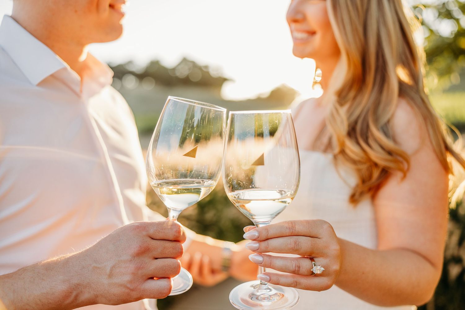 Close-up of hands toasting wine glasses against blurred vineyard background at sunset.