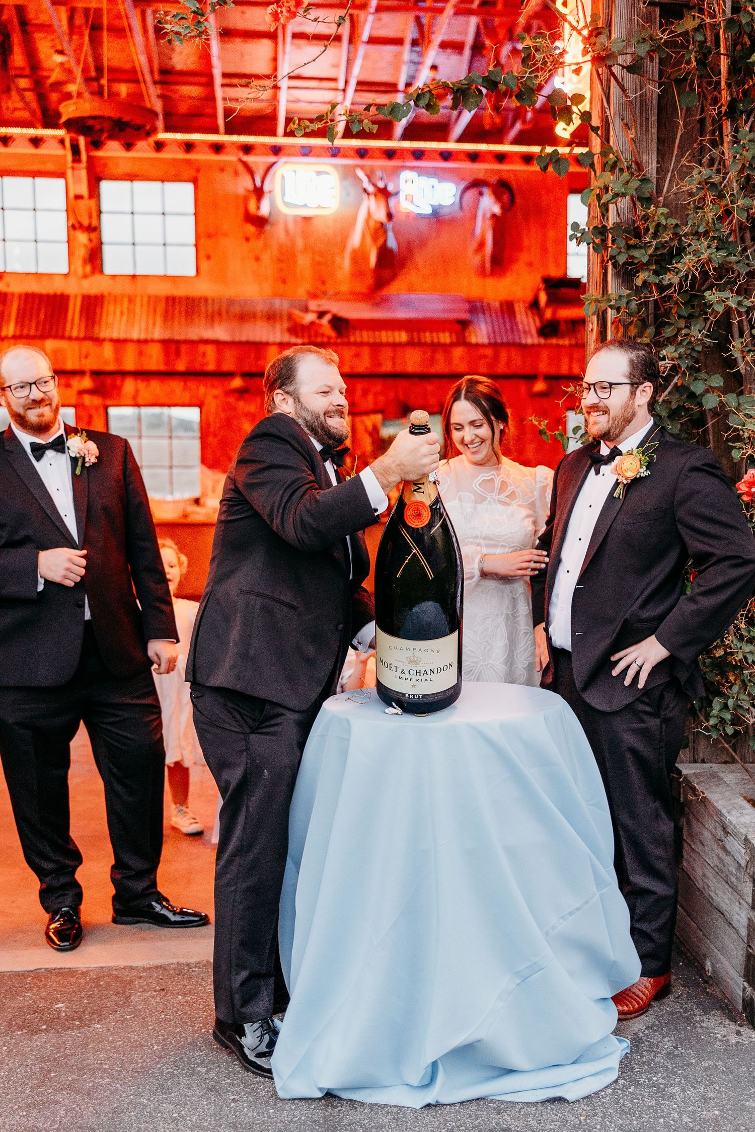 Wedding party celebrates with champagne in a rustic barn venue illuminated with warm red lighting  in San Luis Obispo Holland Ranch.