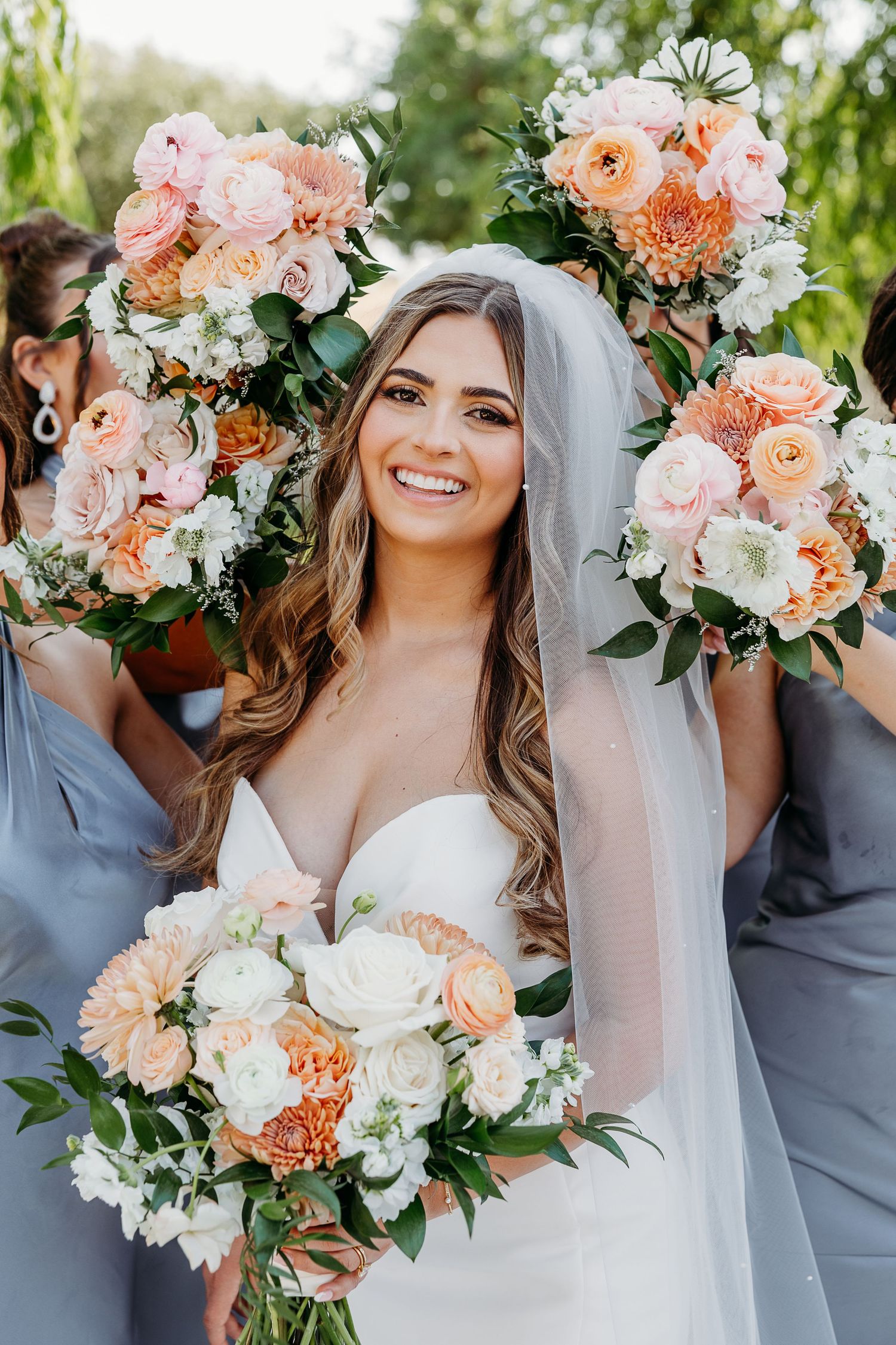 Beautiful wedding bouquets featuring peach and white flowers with greenery against a soft outdoor background.