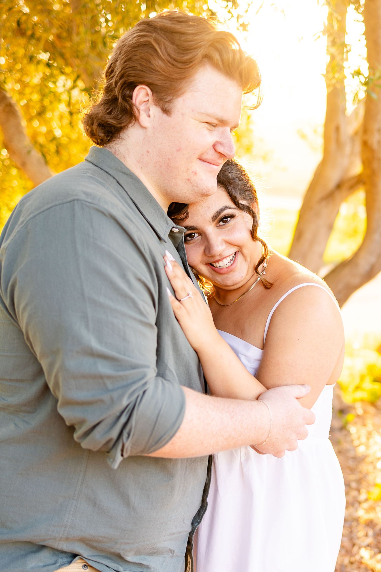 Romantic couple embraces in golden sunlight beneath autumn trees during sunset photoshoot.