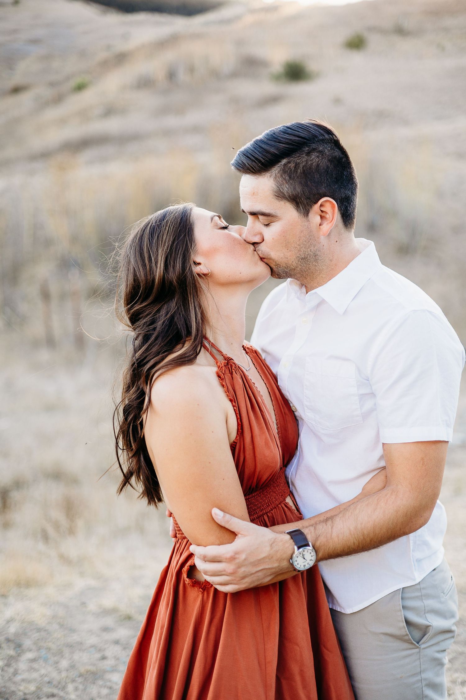 A tender moment shared between a couple against a backdrop of rolling hills.