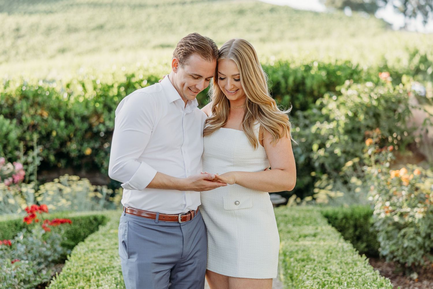 A couple shares a romantic moment together in a lush garden setting during a sunny outdoor photoshoot.