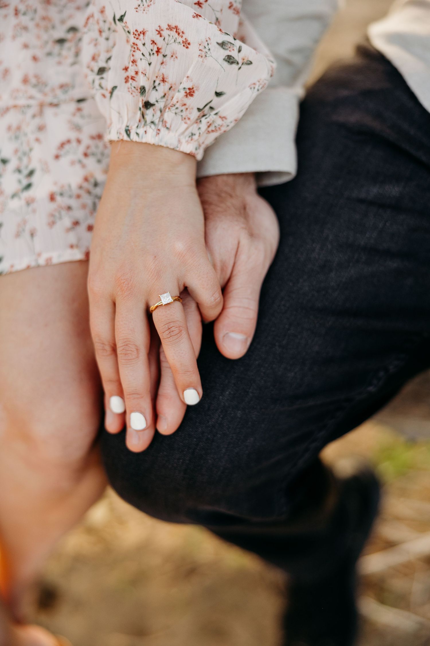Close up of hands together showing an engagement ring with a floral dress sleeve visible.