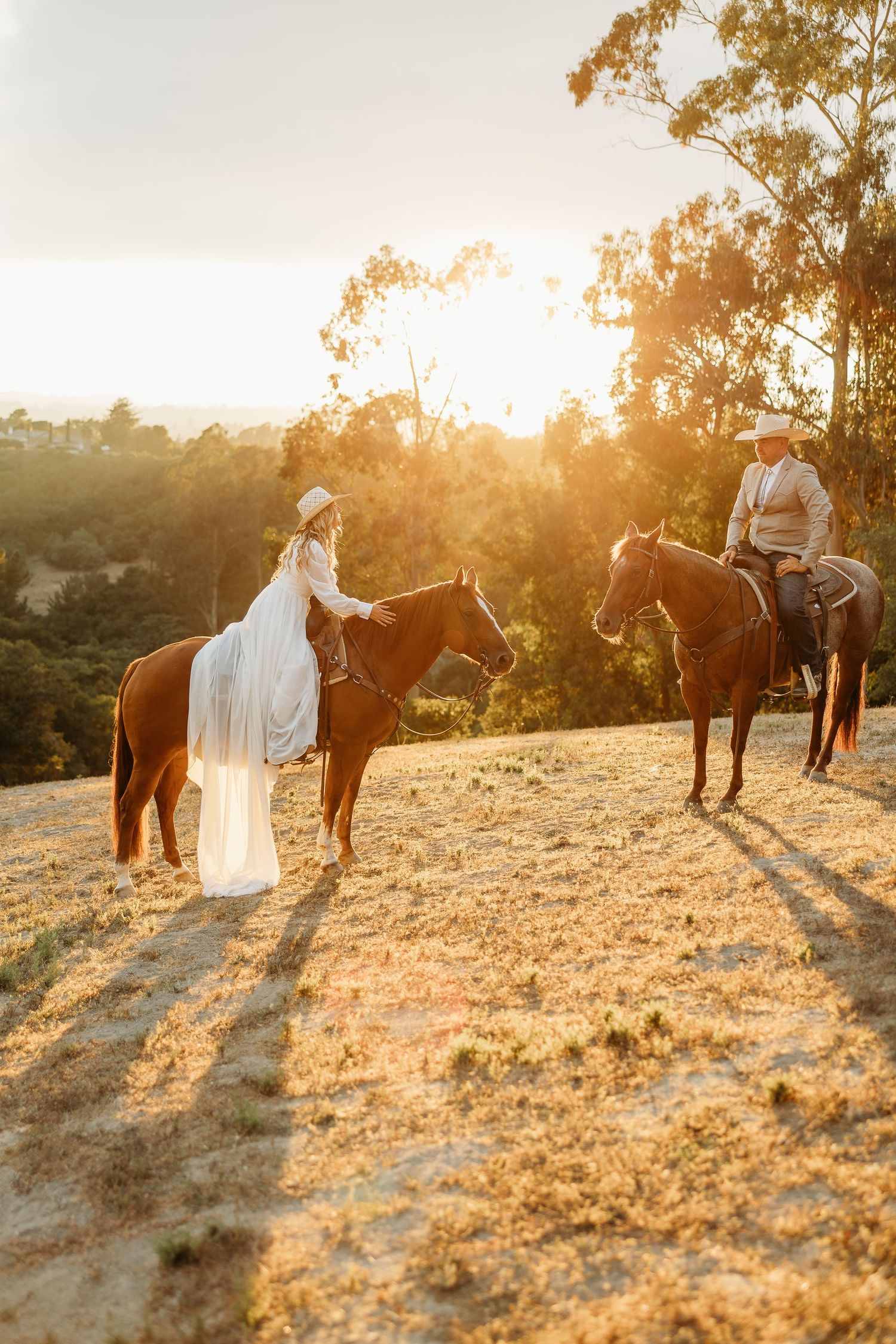 Two riders on horseback pause during a golden sunset on a scenic mountain trail.