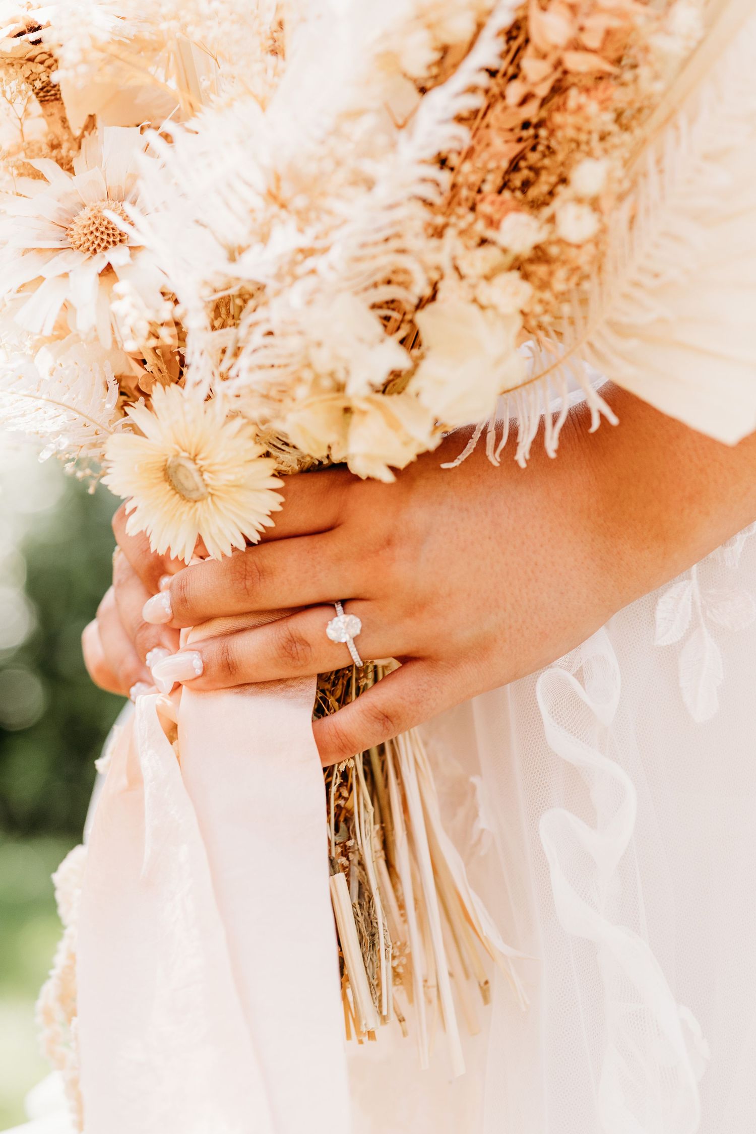 Close-up of hands holding a delicate white wedding bouquet with dried flowers and lace details.