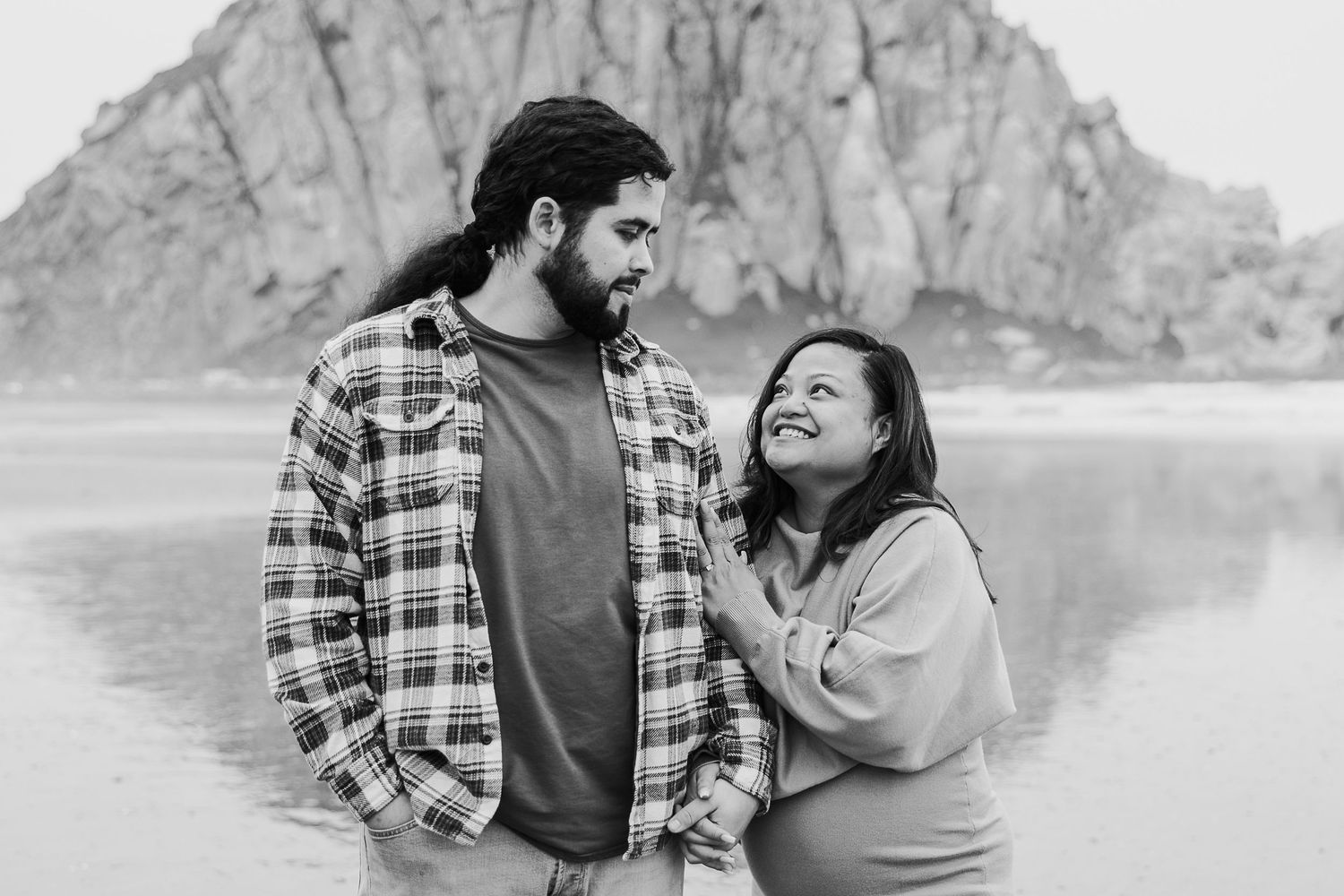 A couple shares a romantic moment while standing together near a scenic mountain lake in black and white.