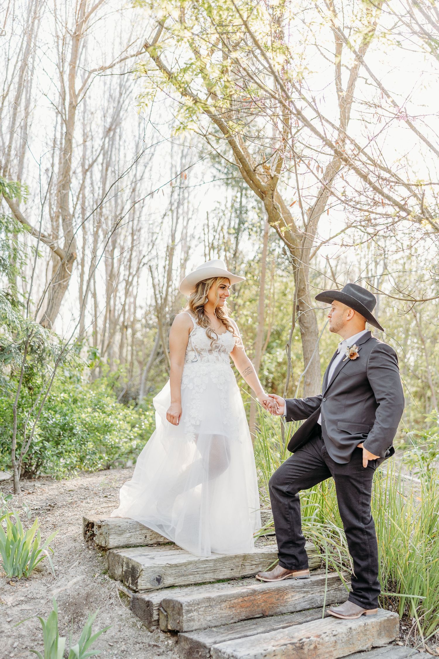 A couple in wedding attire poses on rustic wooden steps surrounded by a dreamy woodland setting.