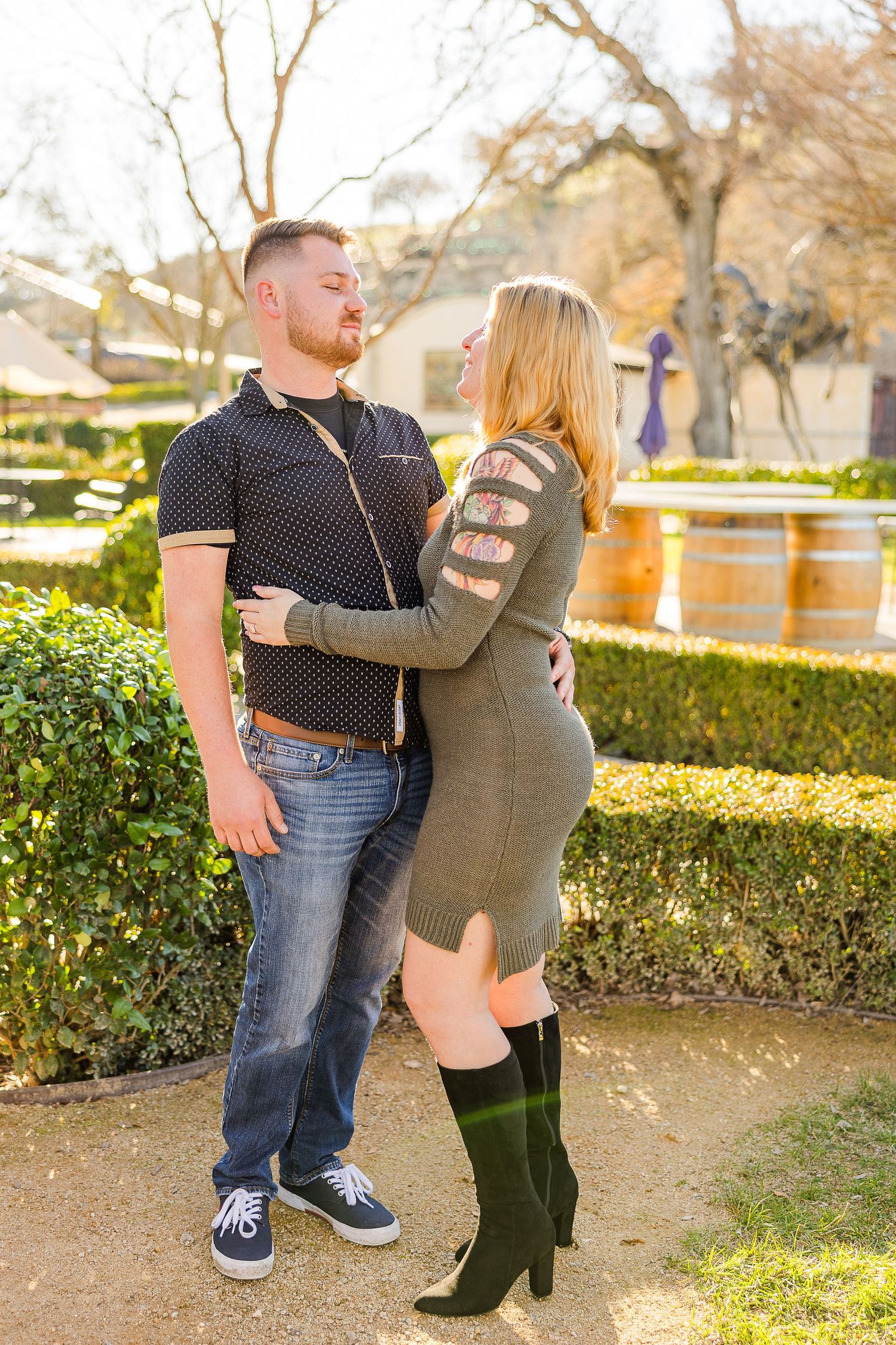 A tender moment between two people at a sunlit winery with decorative landscaping.
