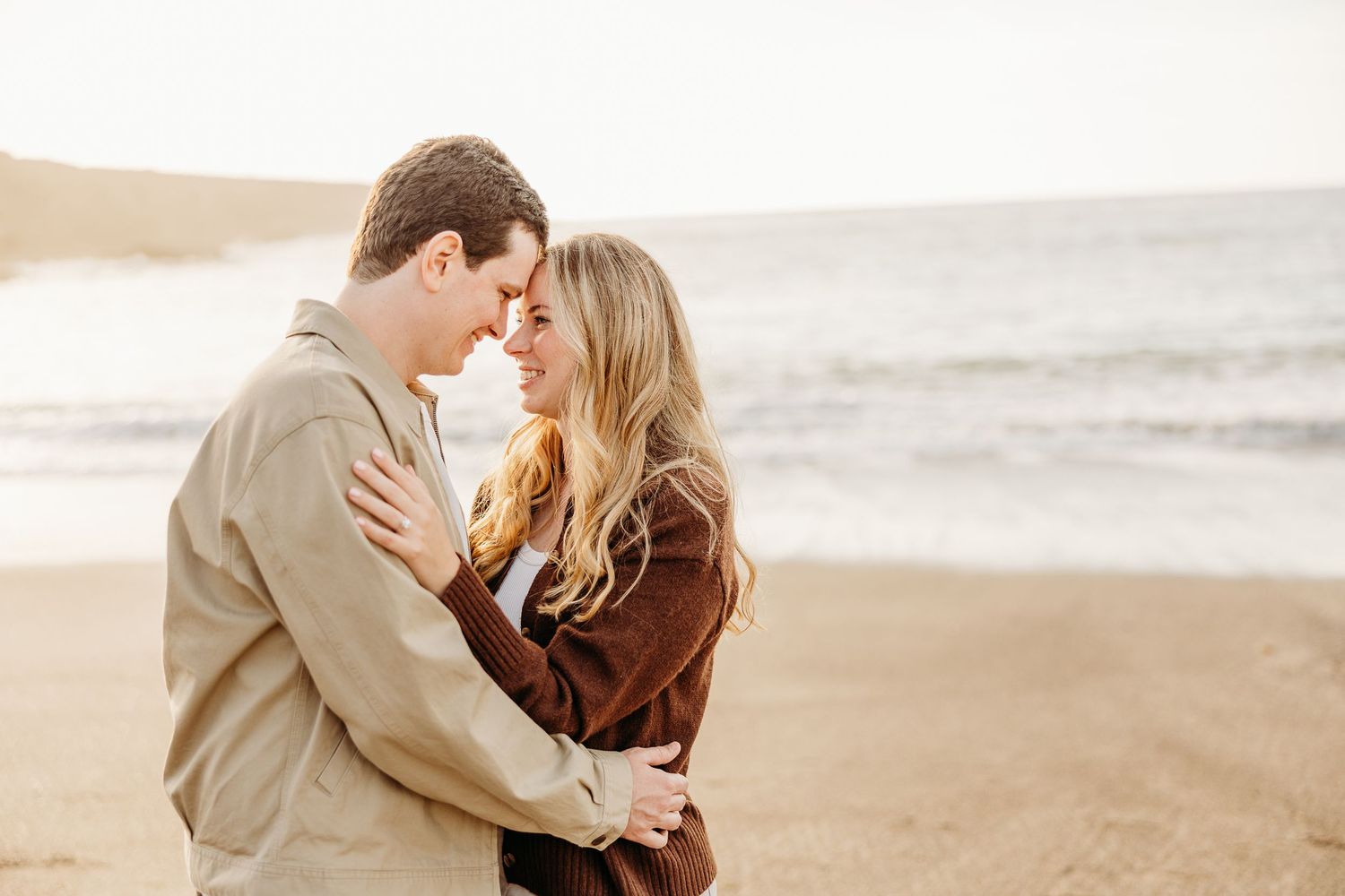 Intimate beach engagement photos with couple embracing against coastal backdrop.