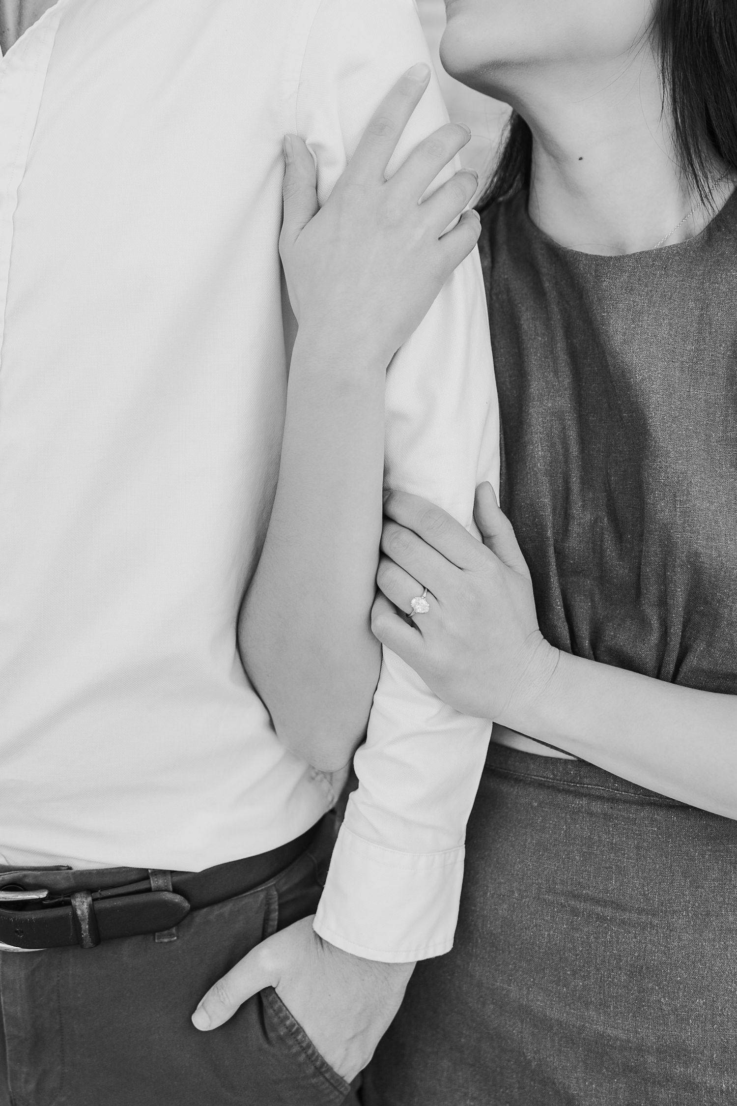 A close-up black and white shot of hands tenderly embracing against white and gray clothing.
