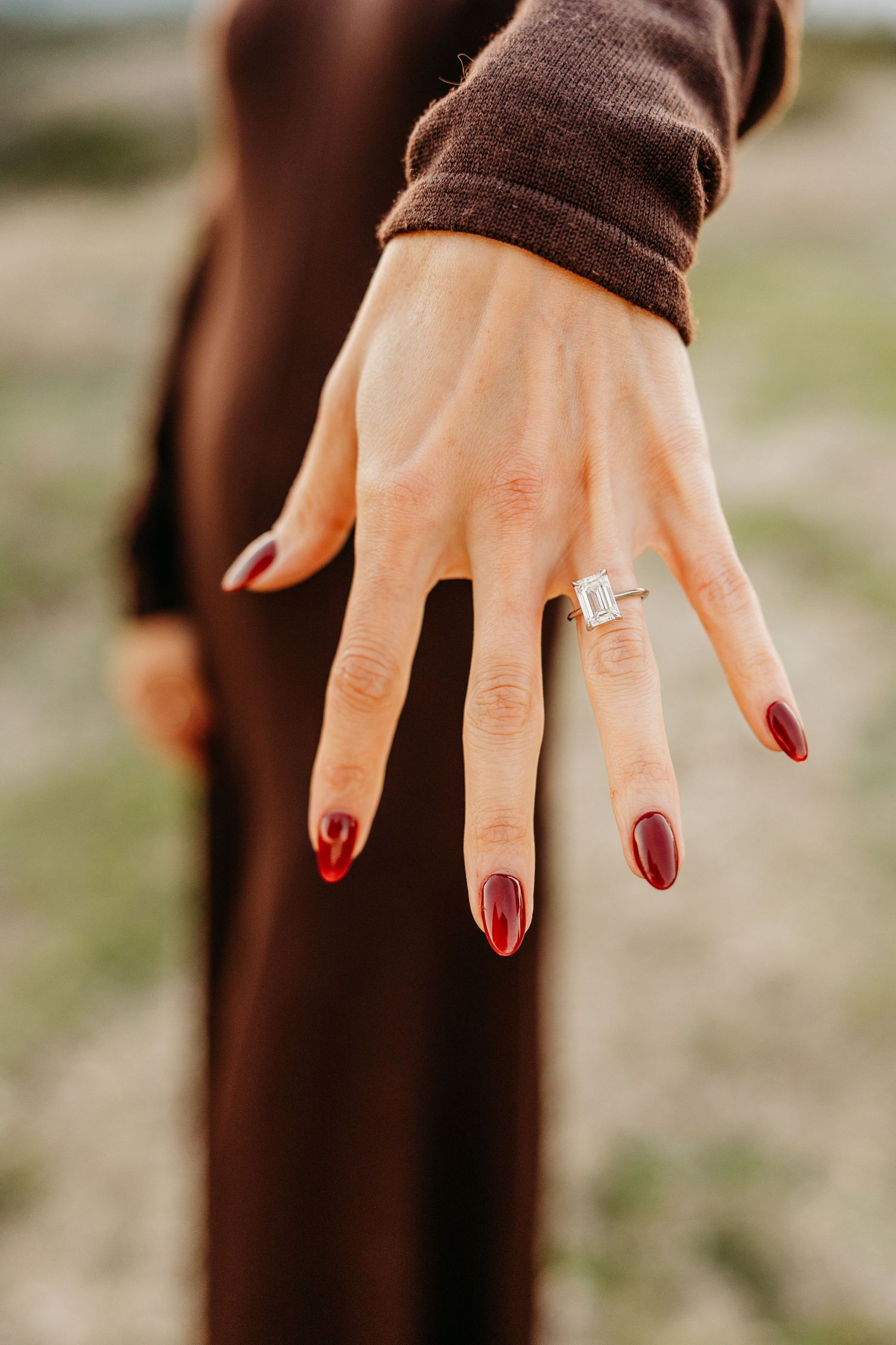 A close-up sequence showing a hand with burgundy red nail polish wearing an elegant engagement ring against a brown background.