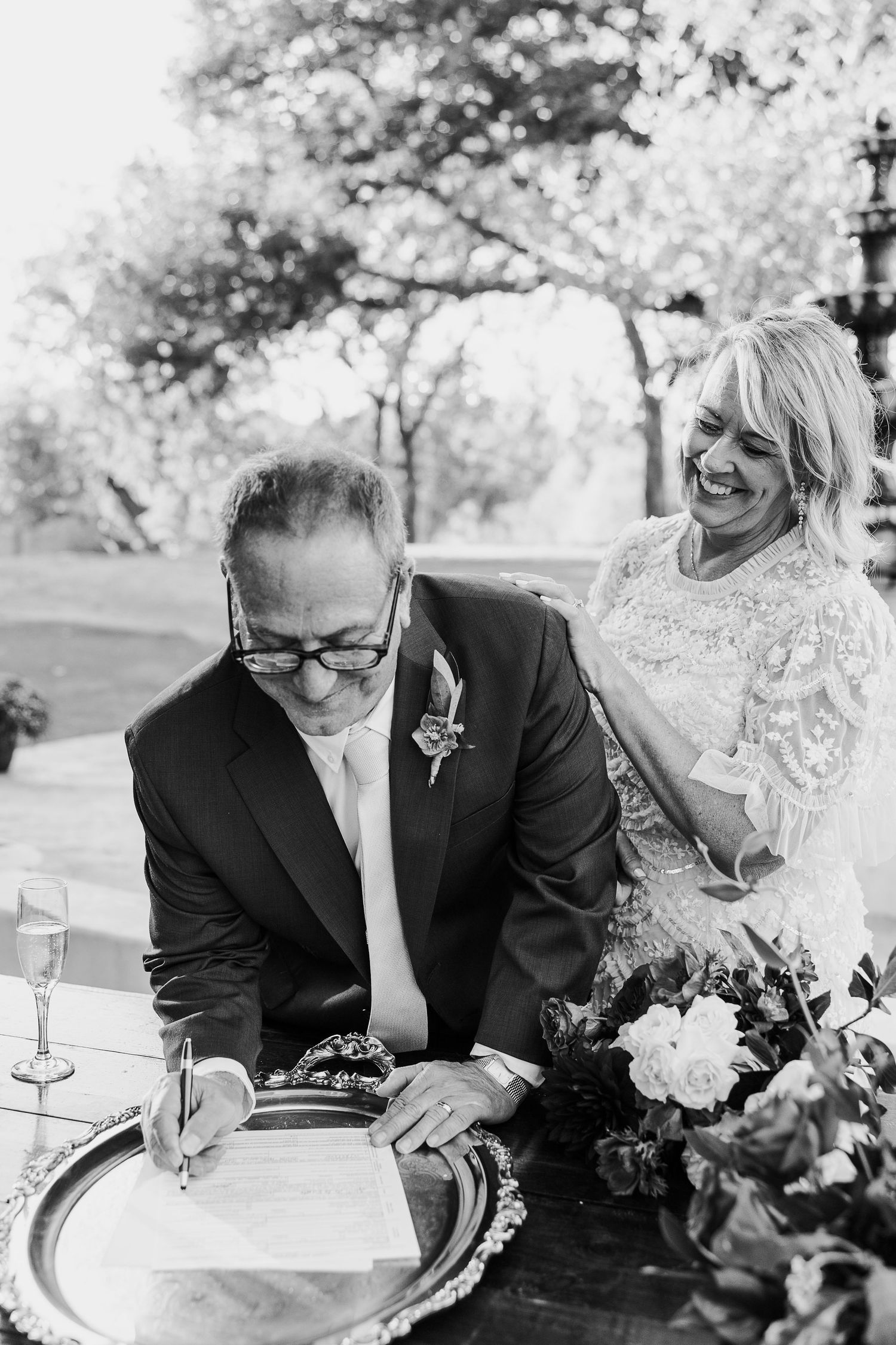 Black and white photos of couple signing documents at outdoor wedding ceremony.