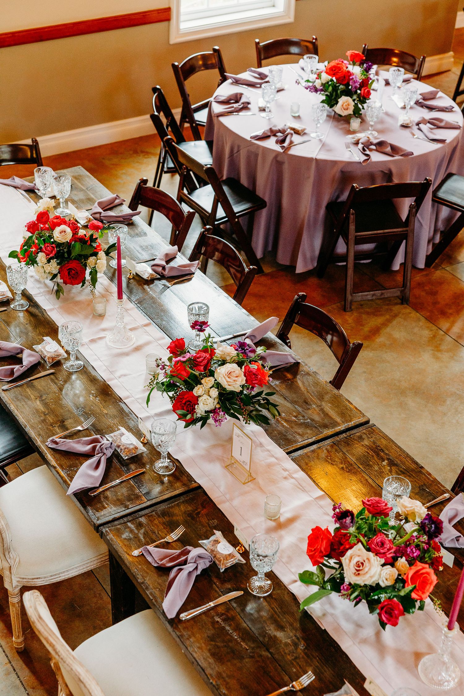 Elegant wedding reception tables decorated with red and white floral centerpieces and brown wooden chairs.