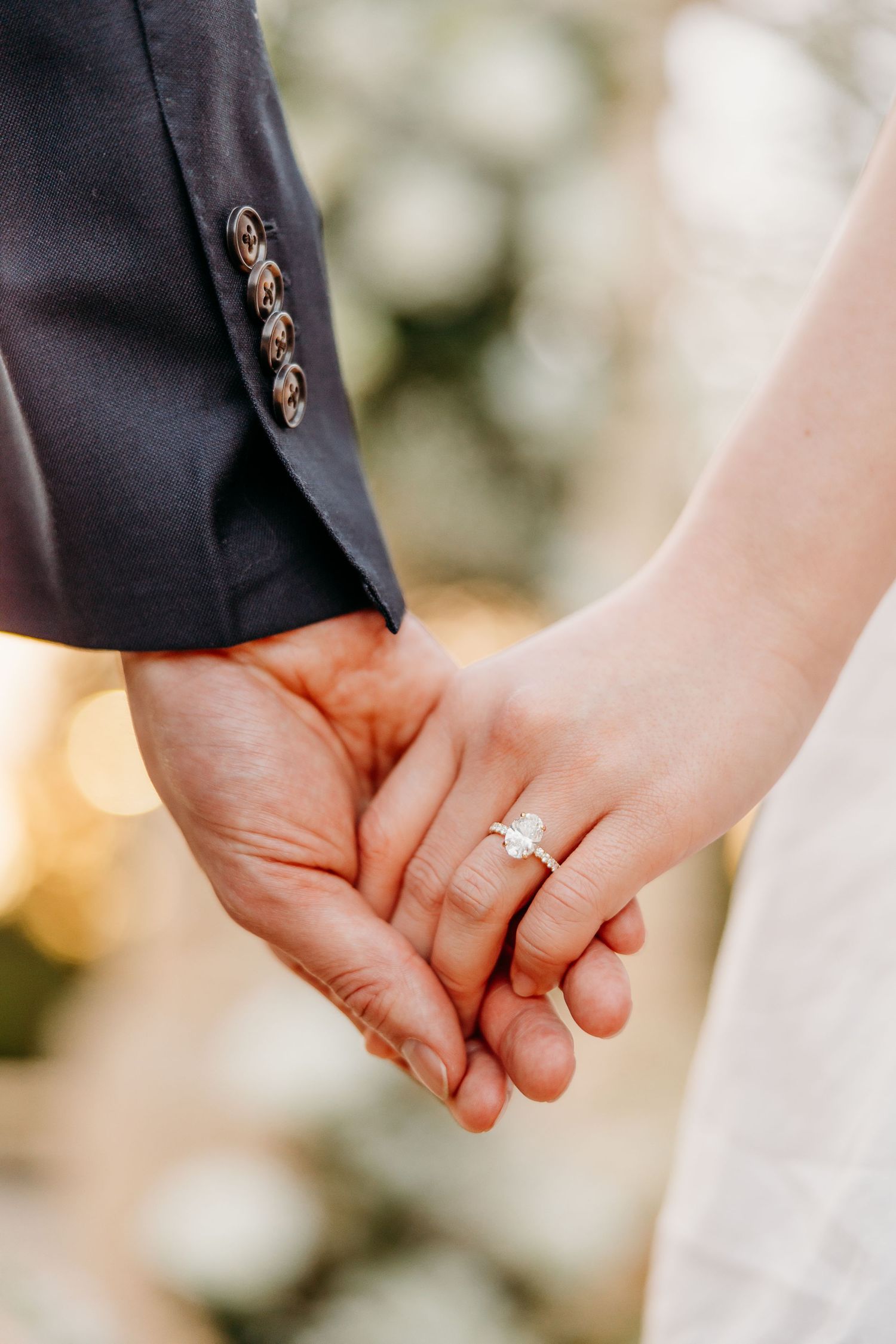 Close-up of couple holding hands showing engagement ring in outdoor setting.