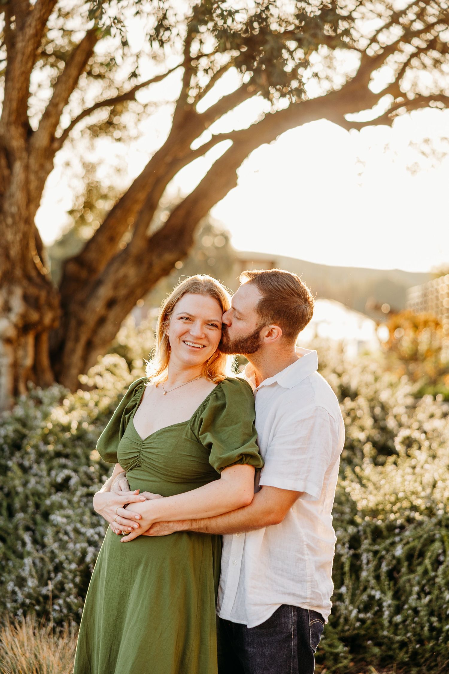 A couple embraces under golden sunlight filtering through tree branches.