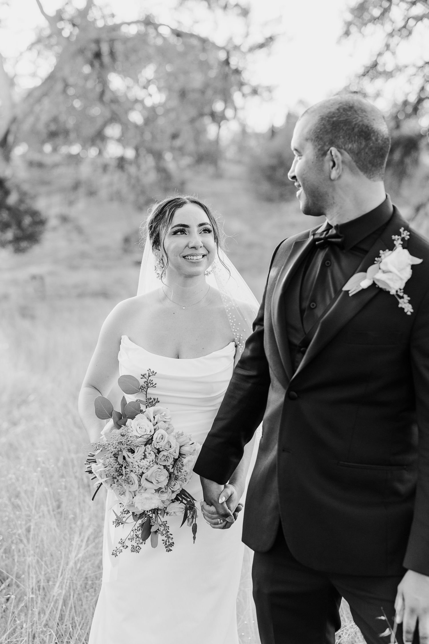 Black and white photo series of couple in wedding attire walking through field.