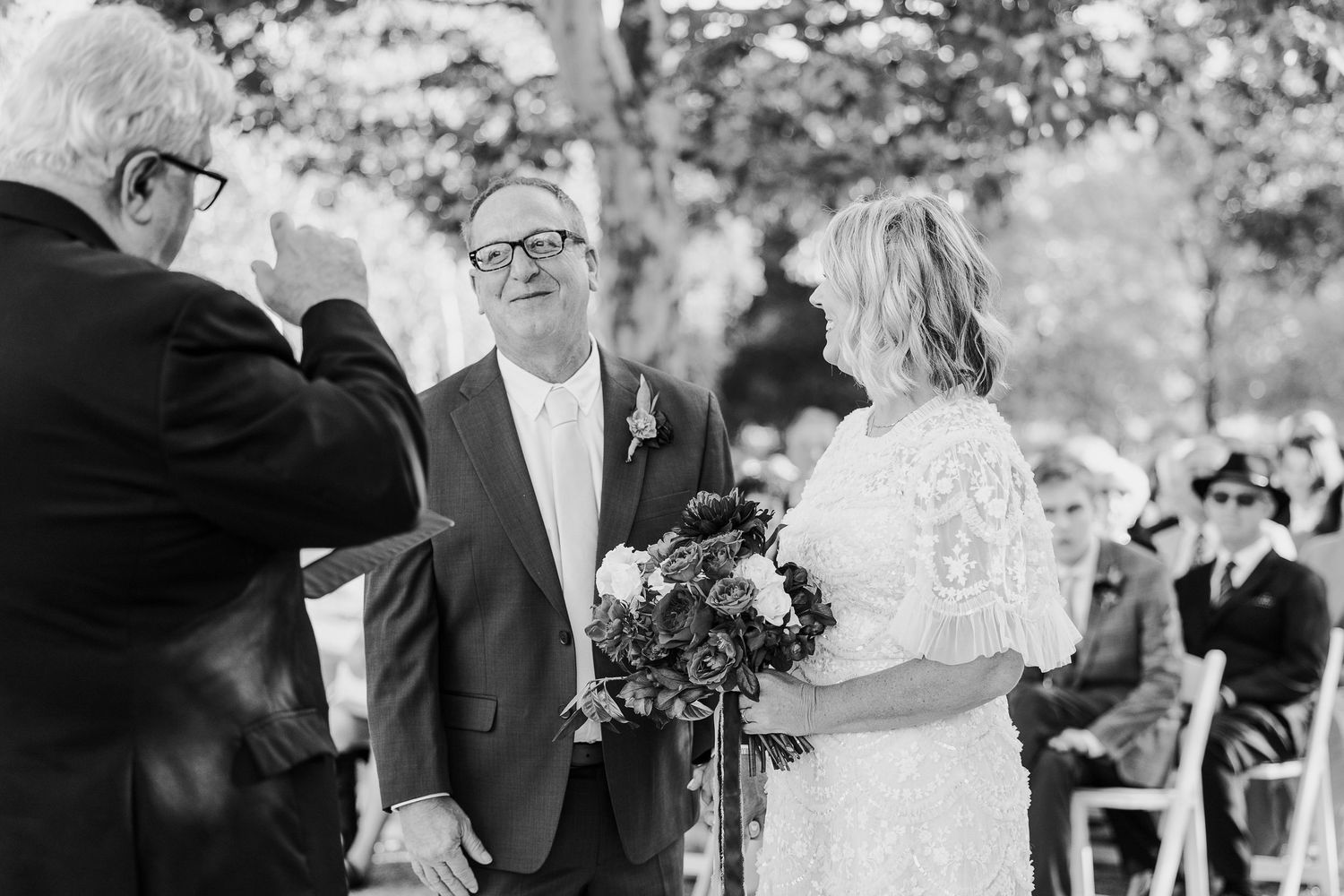 Outdoor wedding ceremony with guests seated in rows under trees.