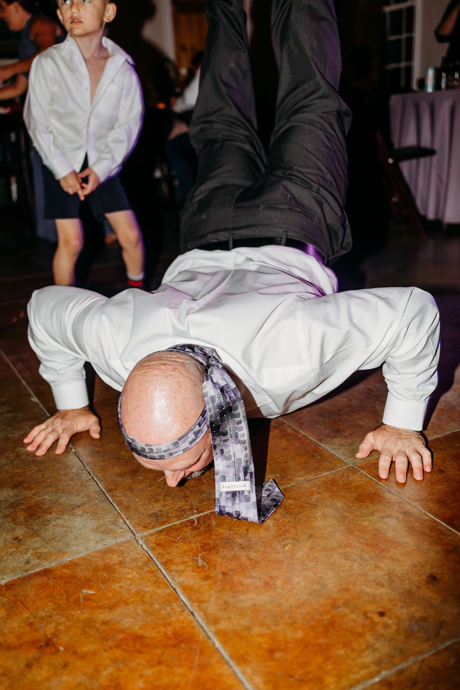 Wedding guest performing breakdance moves on reception dance floor.