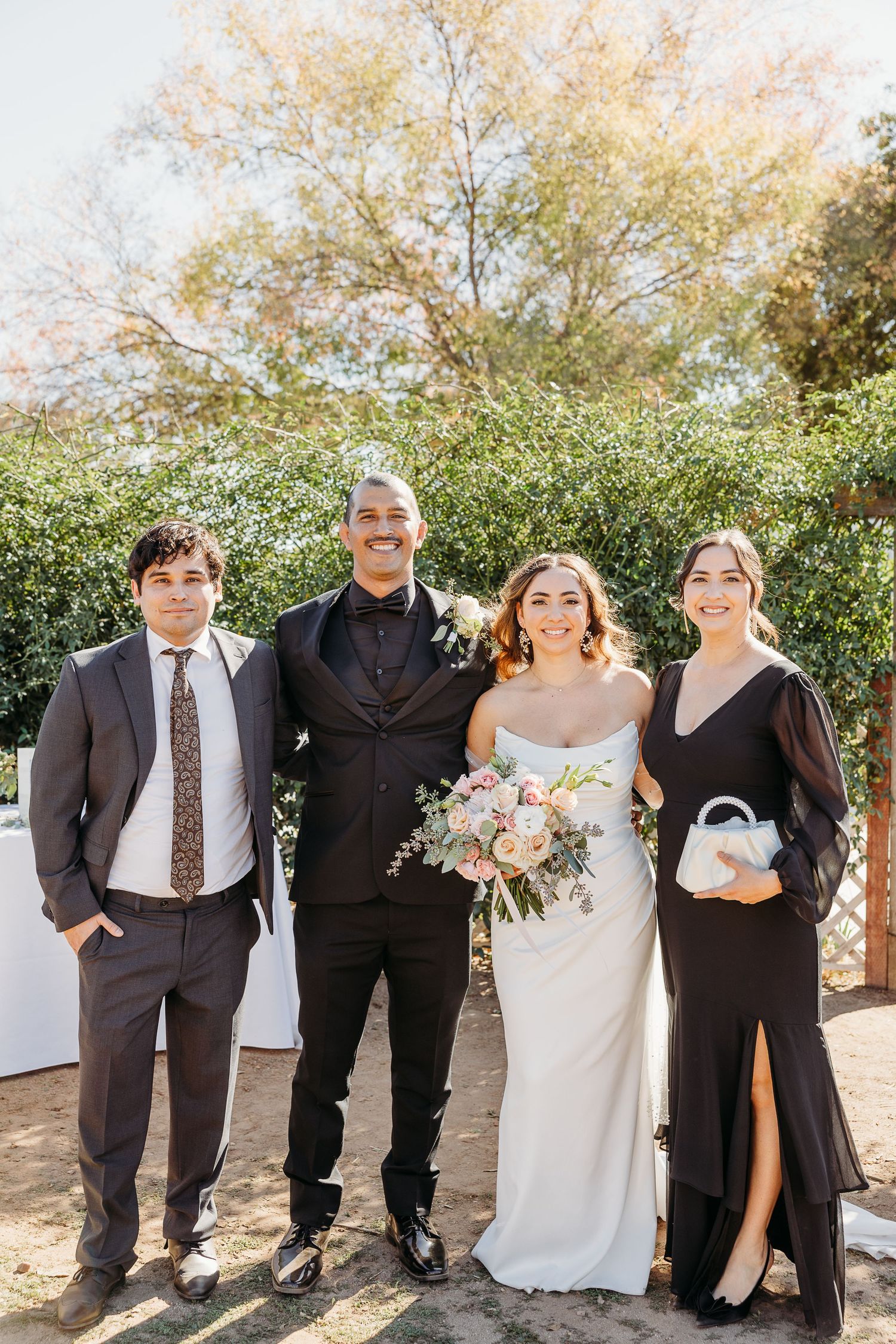 Wedding party in formal attire poses outdoors against autumn foliage.