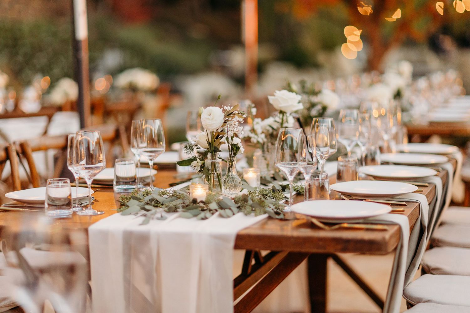Rustic wedding reception tables decorated with eucalyptus garlands and warm ambient lighting.