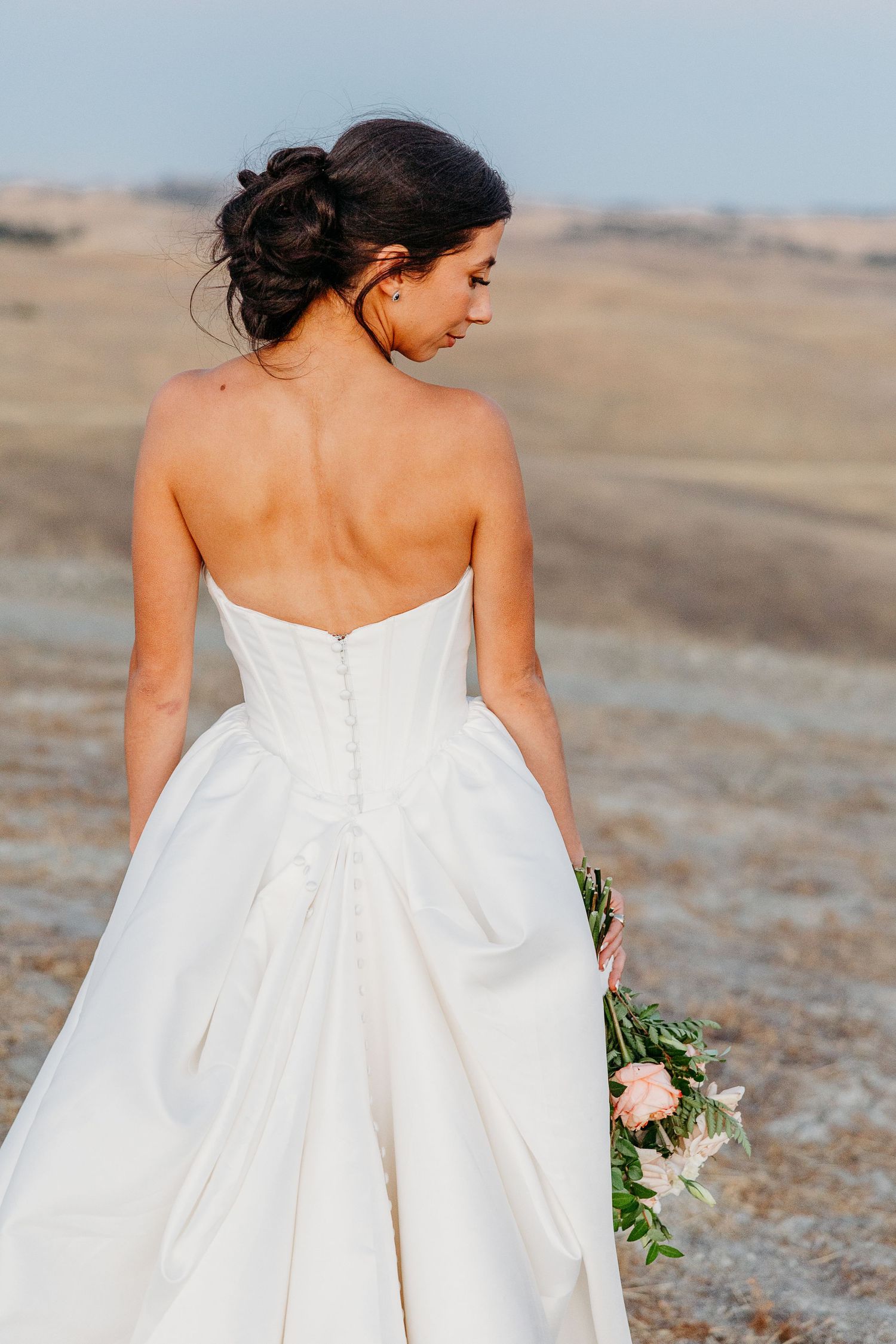 Back view of a strapless white wedding dress with button details against a desert landscape.
