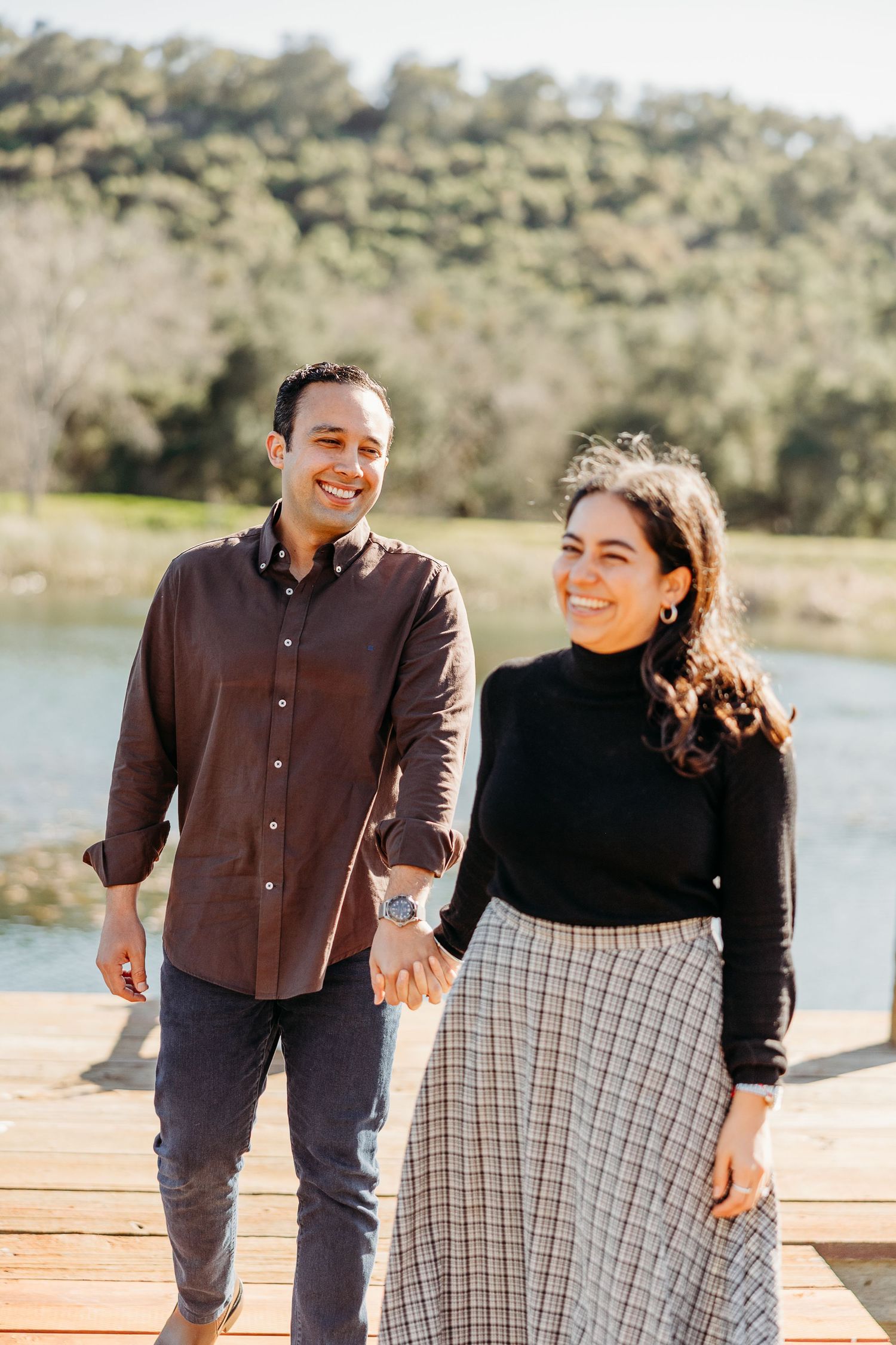 A couple standing together on a wooden deck with hills and nature in the background on a sunny day.