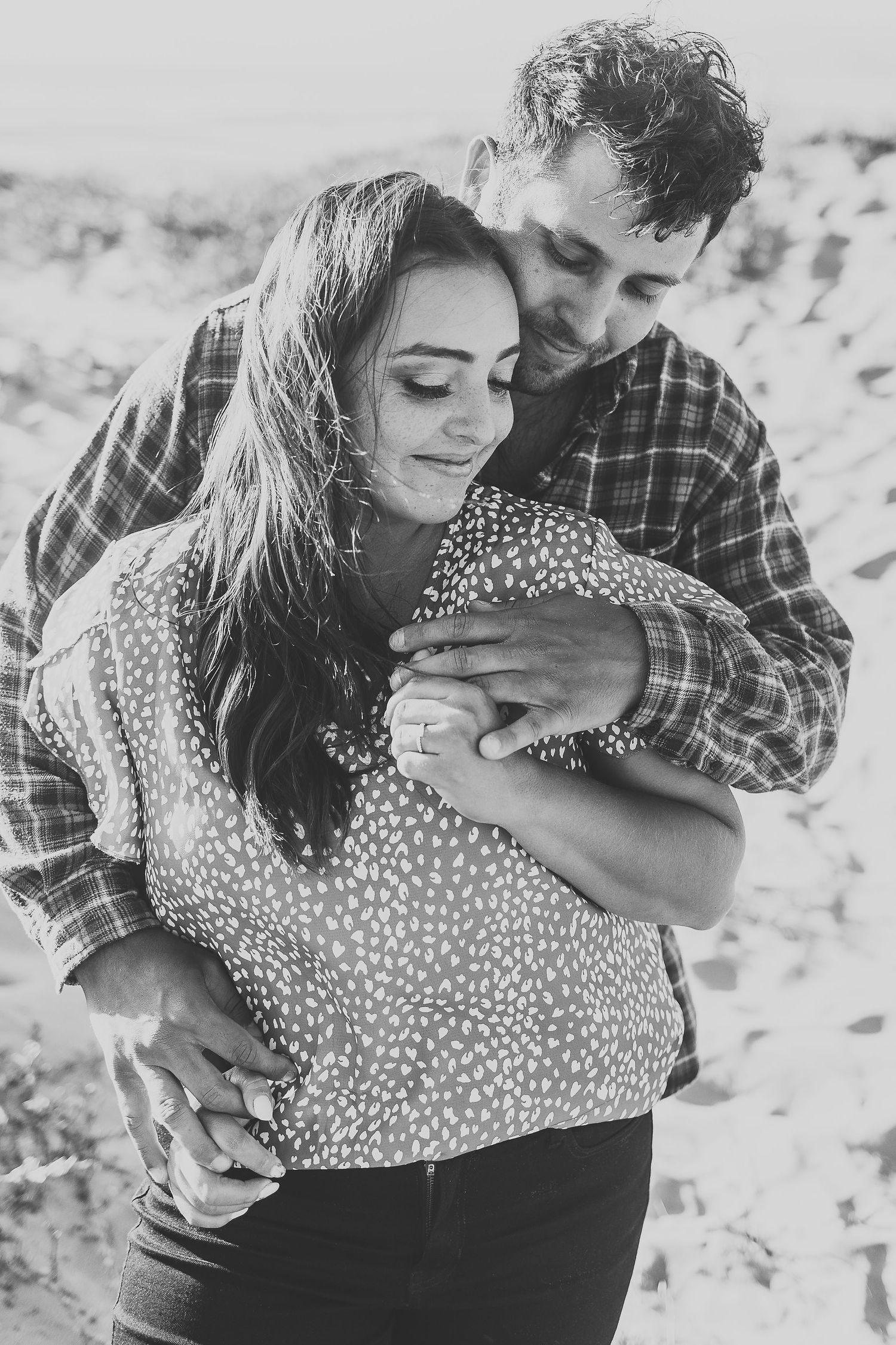 Intimate black and white portrait of couple hugging on beach dunes.