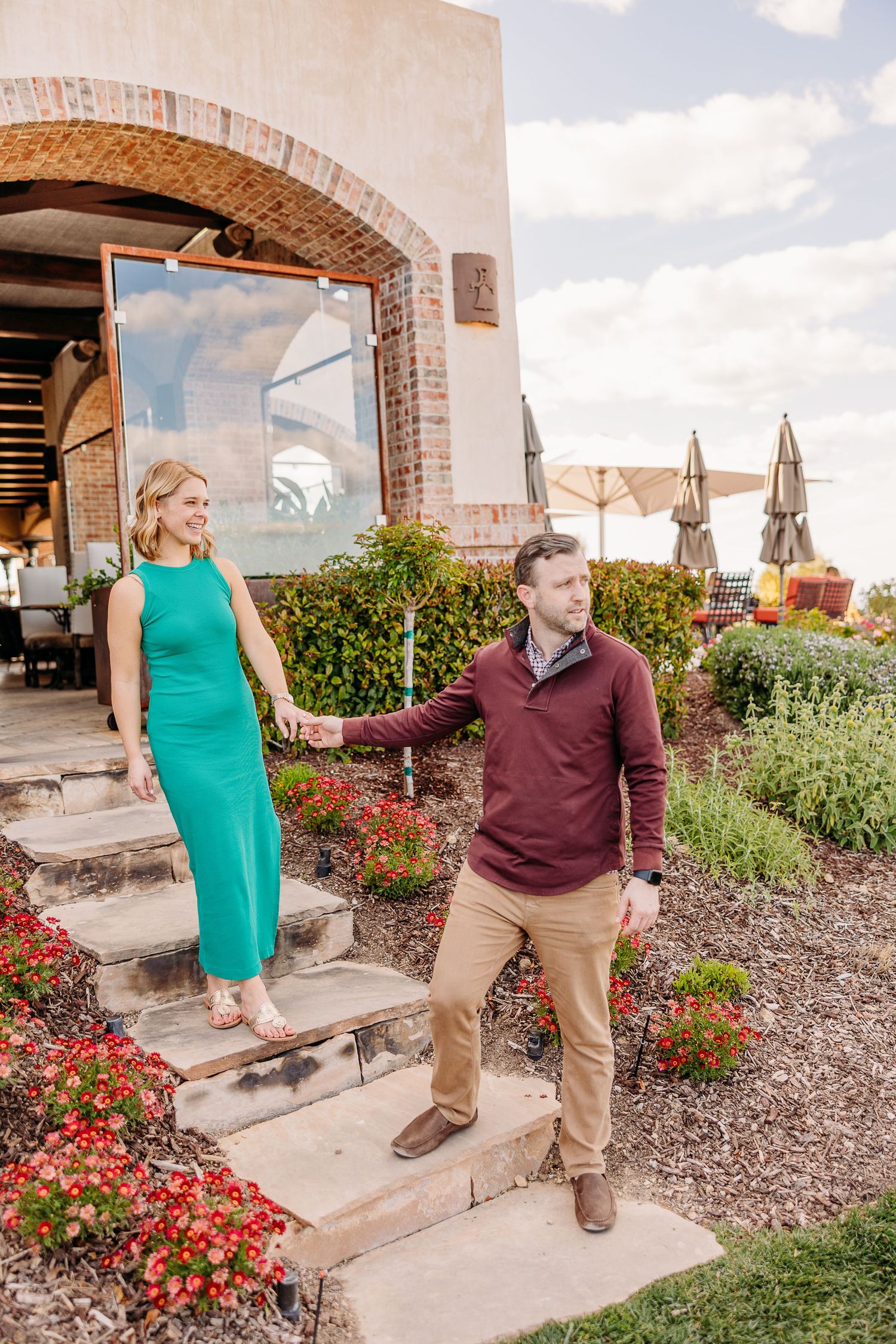 Couple takes romantic photos in front of a brick building with colorful flower gardens.