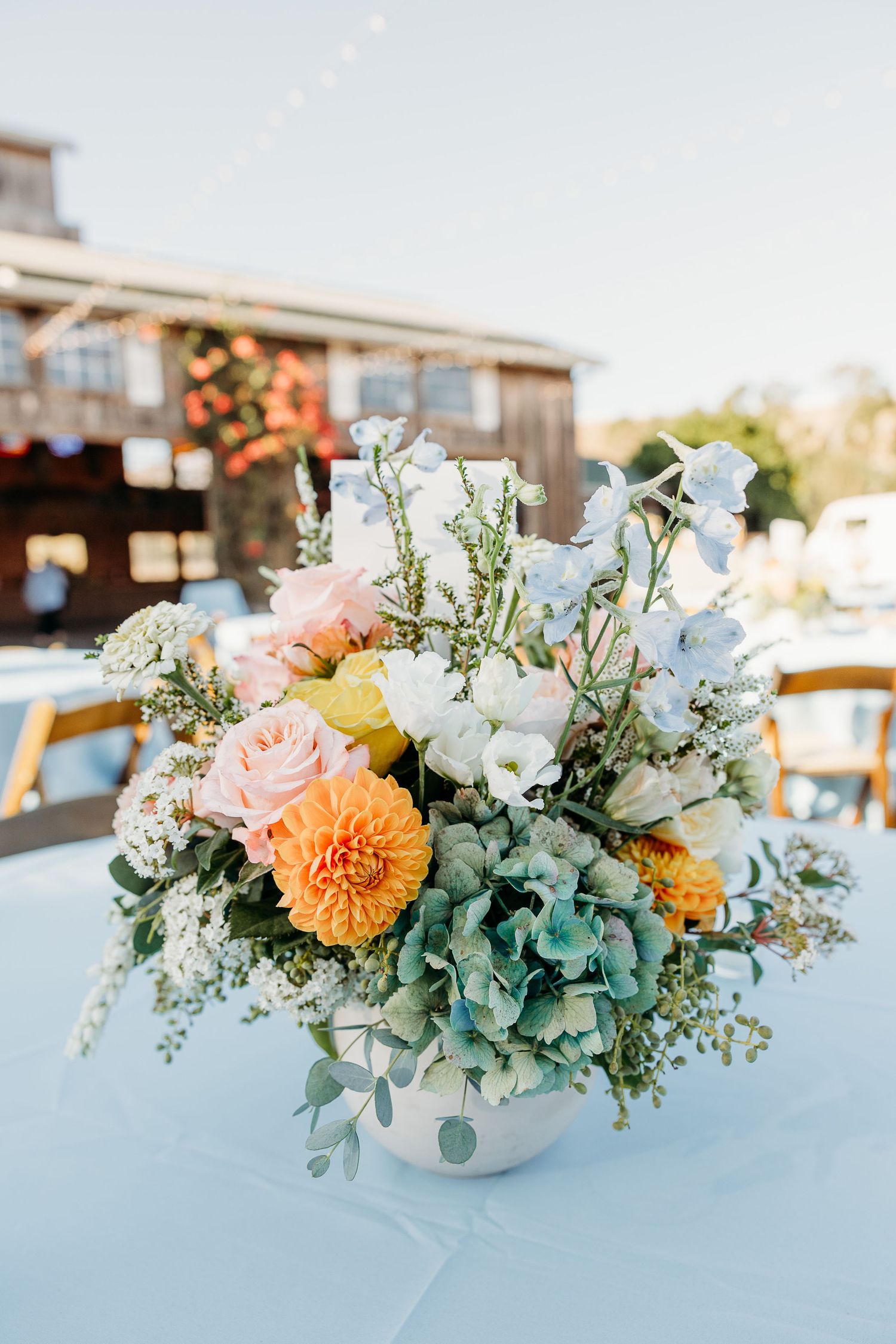 Elegant floral centerpiece with peach, orange and white flowers on light blue tablecloth at Holland Ranch San Luis Obispo