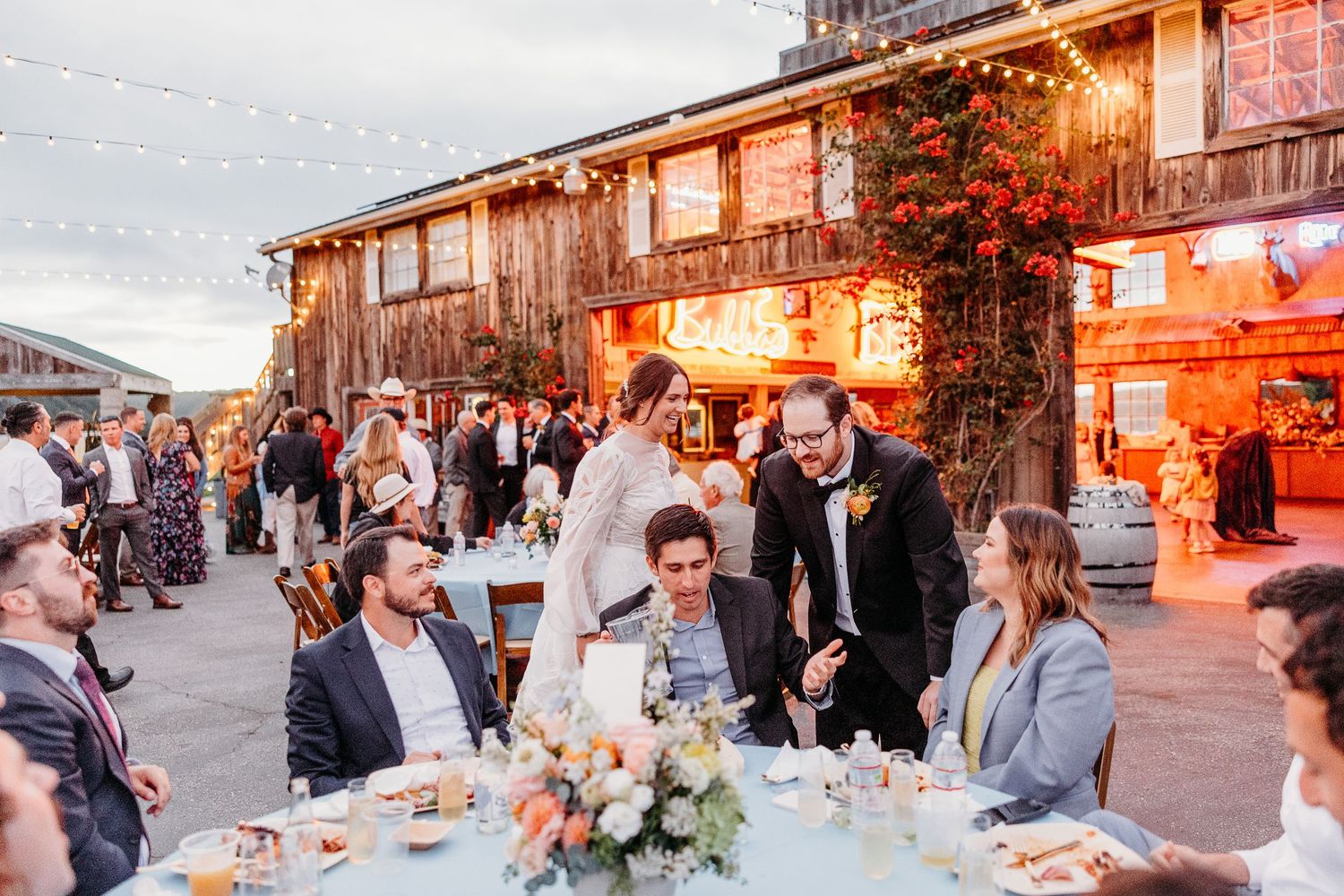 Rustic outdoor wedding reception with guests dining at tables near barn at sunset at Holland Ranch SLO.