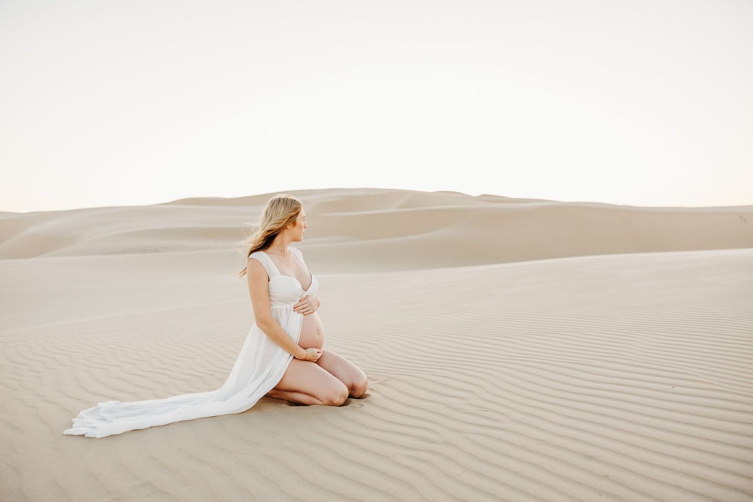 Ethereal maternity session with flowing white fabric in desert sand dunes.