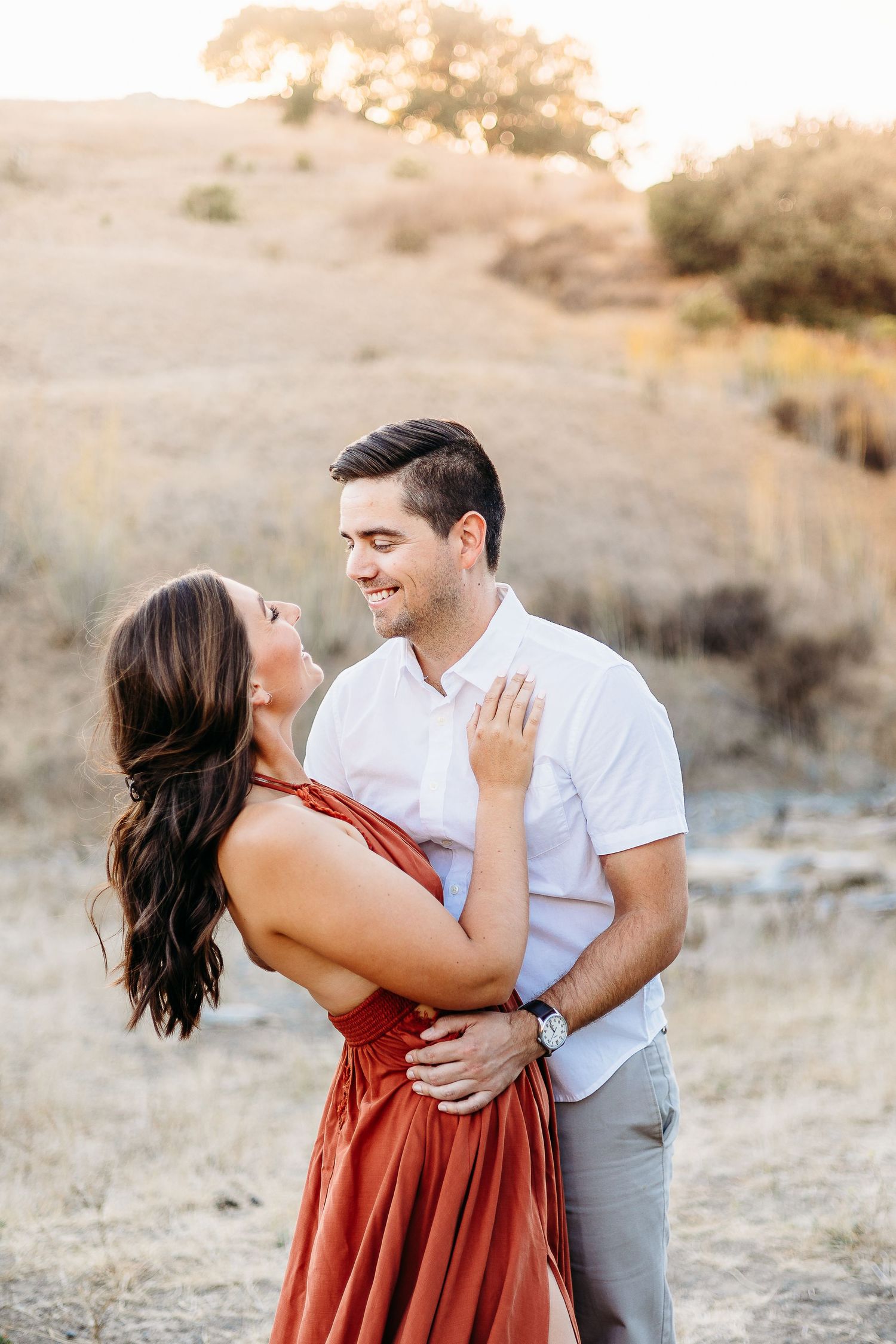 A couple shares an intimate moment against a backdrop of rolling hills during golden hour.