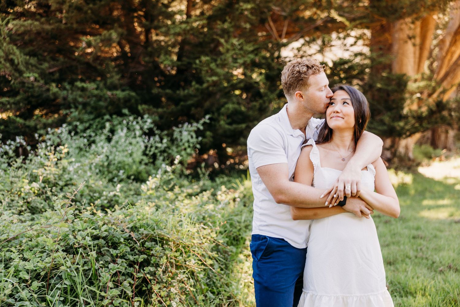 A couple embraces in a romantic pose surrounded by lush greenery and natural afternoon light.
