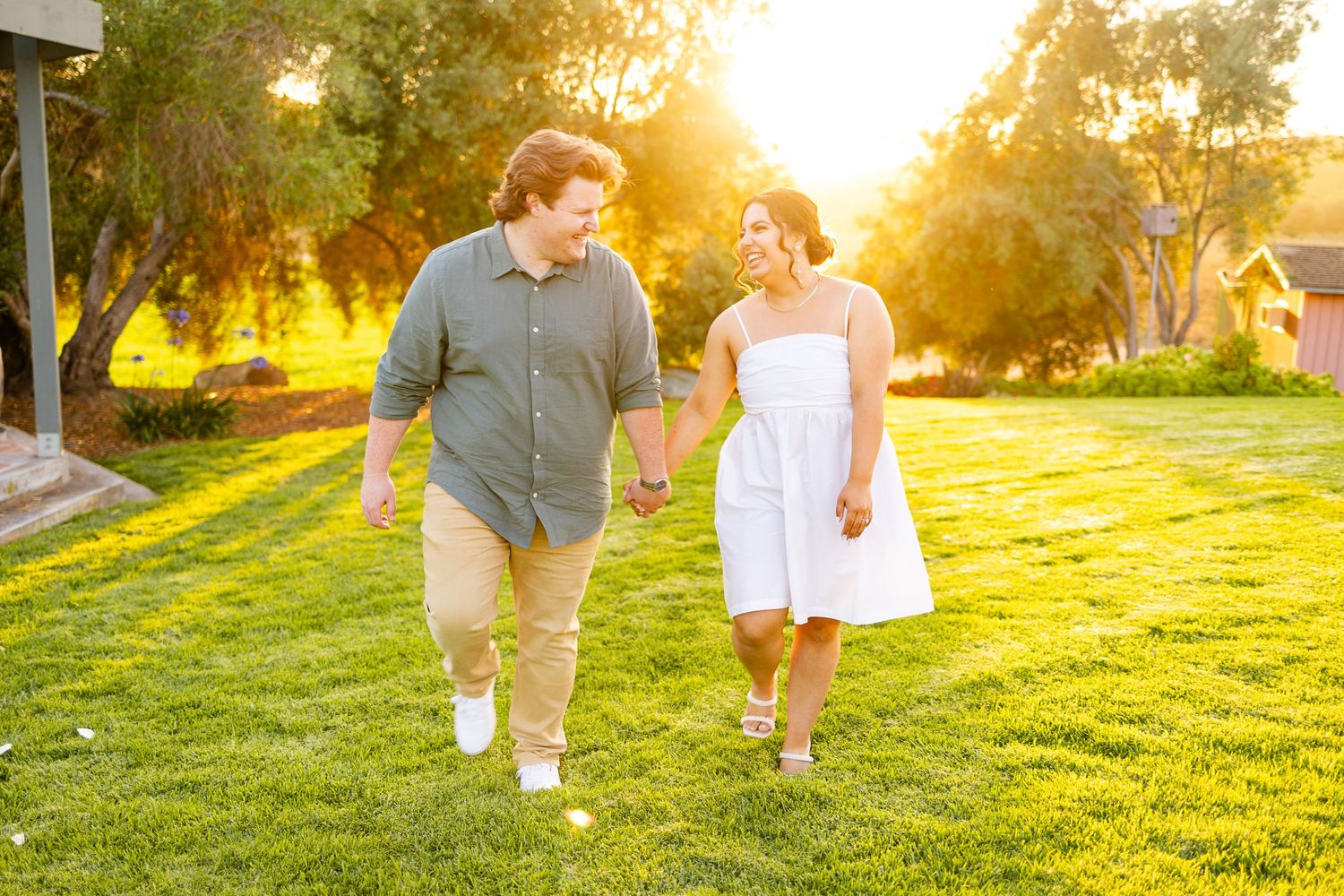 Couple holding hands while walking on sunny green lawn during golden hour.