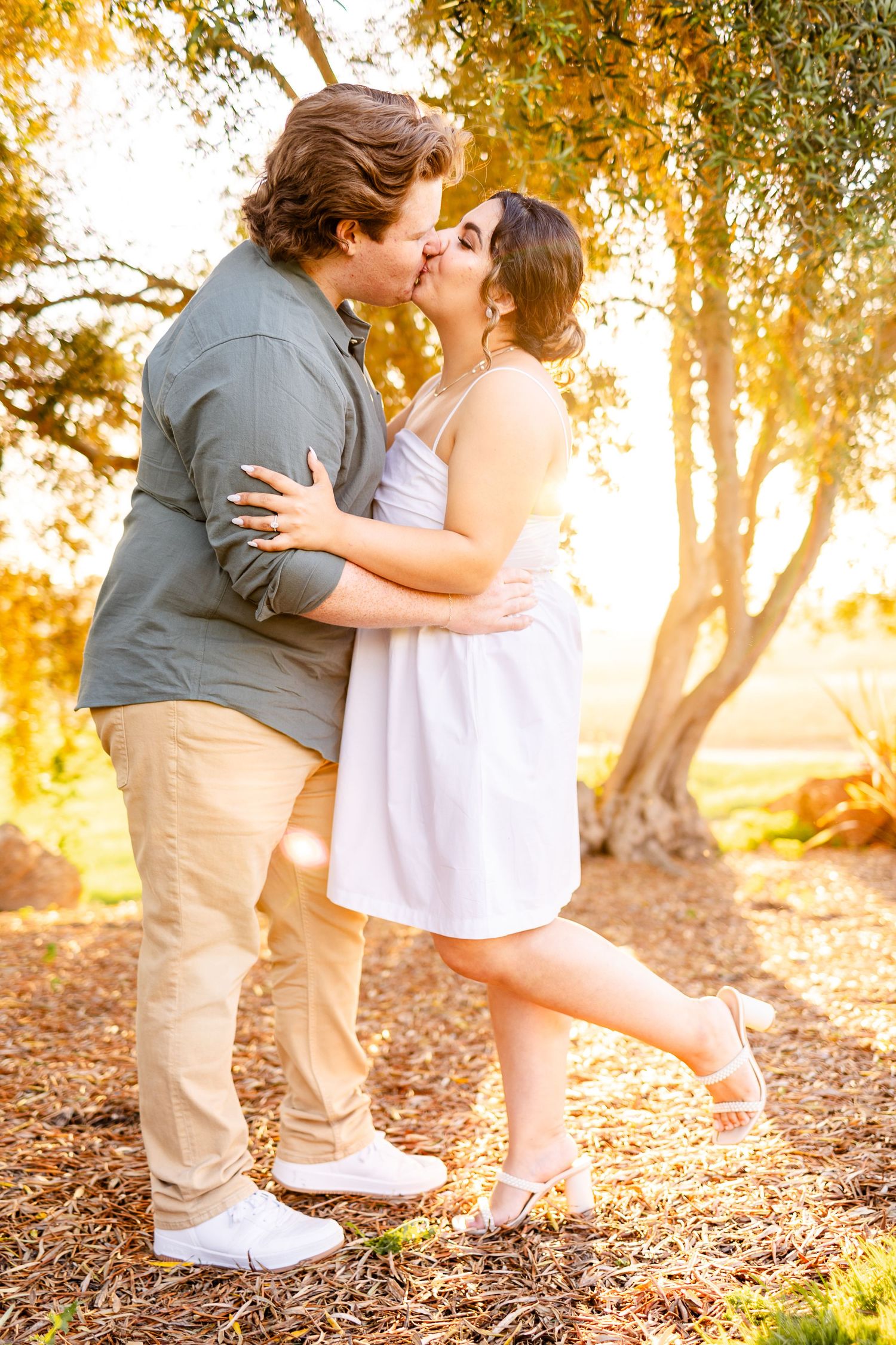 A romantic kiss captured during golden hour beneath autumn trees.