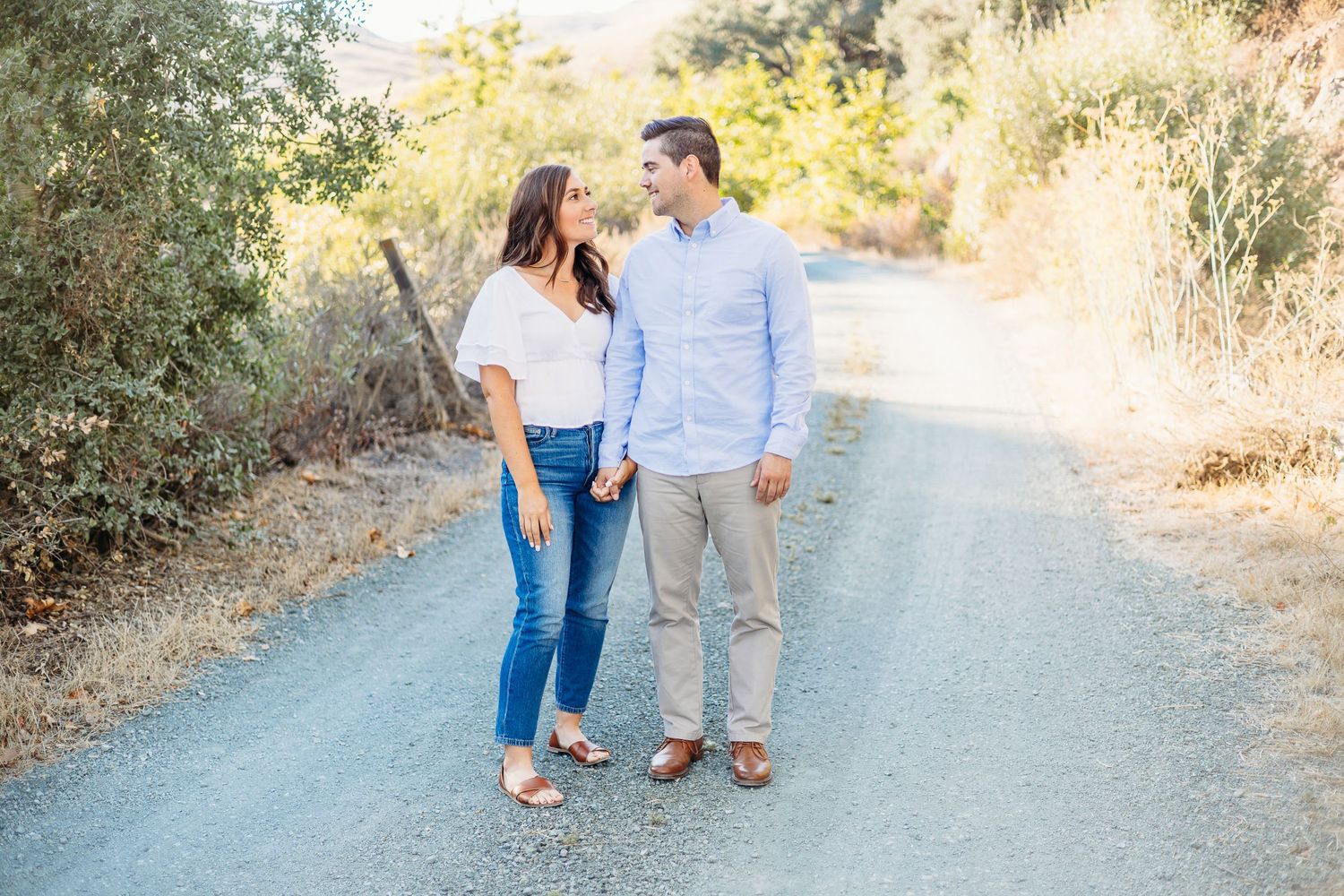 A couple walking together on a dirt path surrounded by nature in casual outfits.