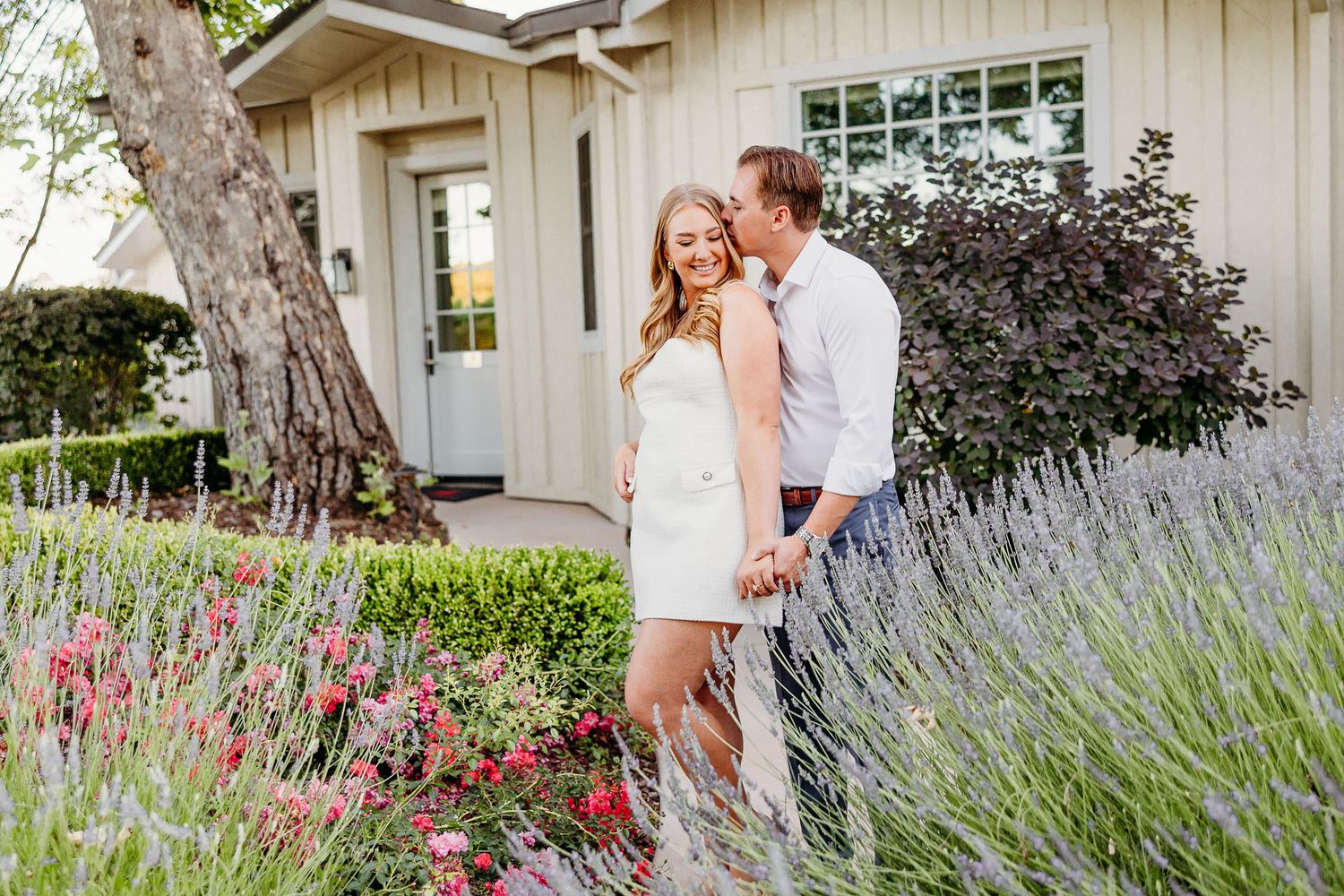 A romantic outdoor photoshoot in front of a white house with blooming lavender and garden flowers.