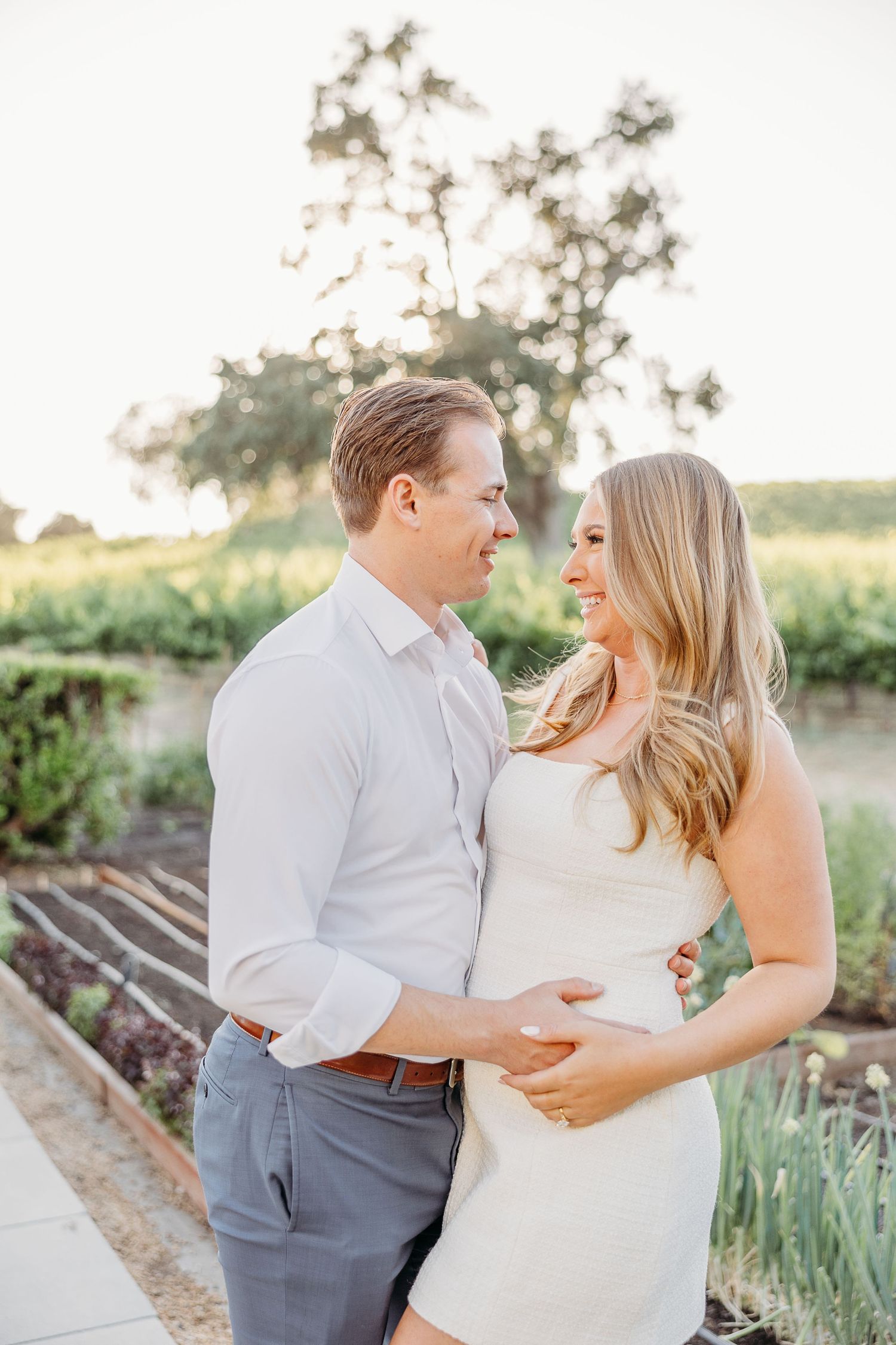 A couple embraces and laughs together in a garden setting during their engagement or wedding photo session.