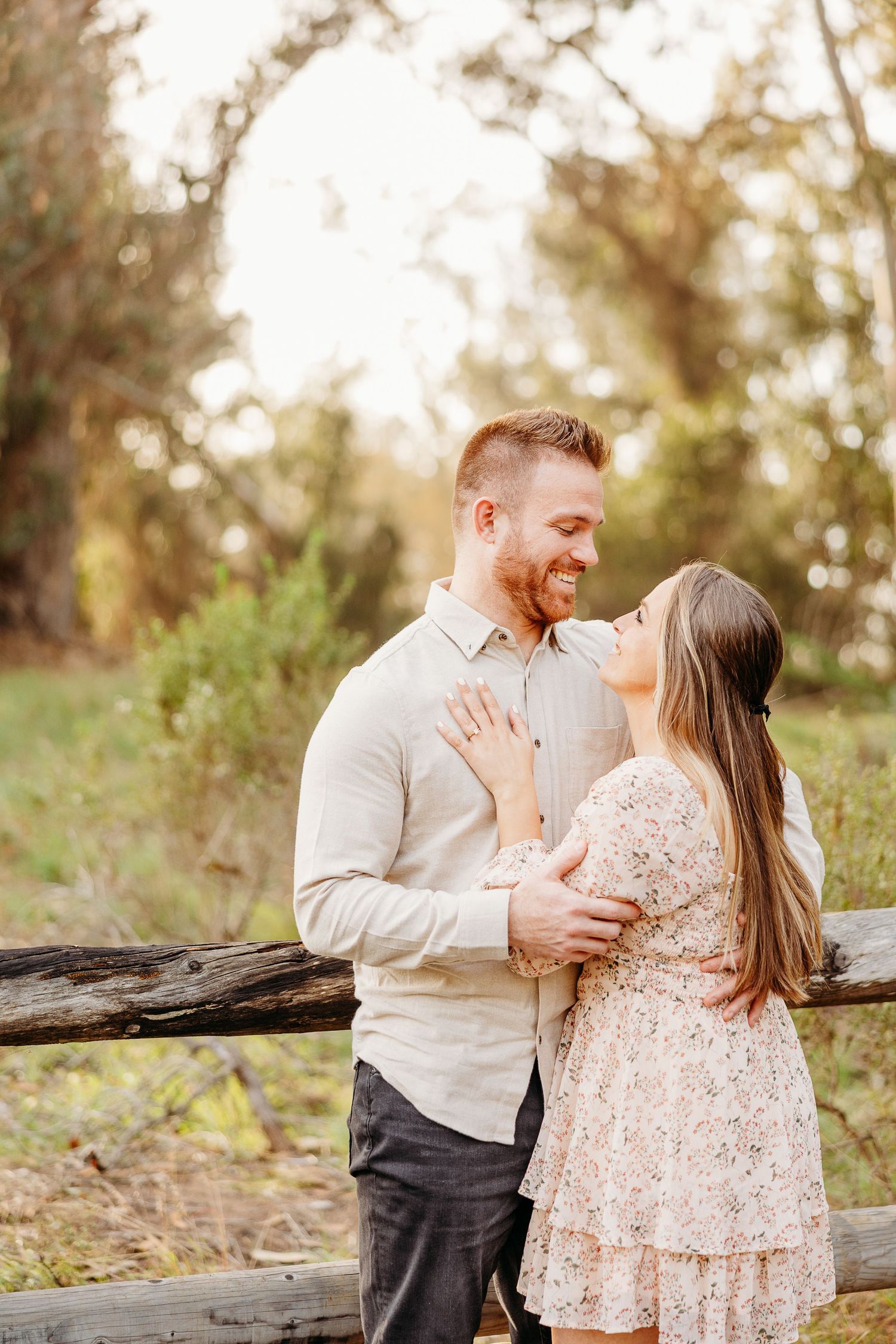 Couple sharing romantic moment by rustic wooden fence in natural setting.