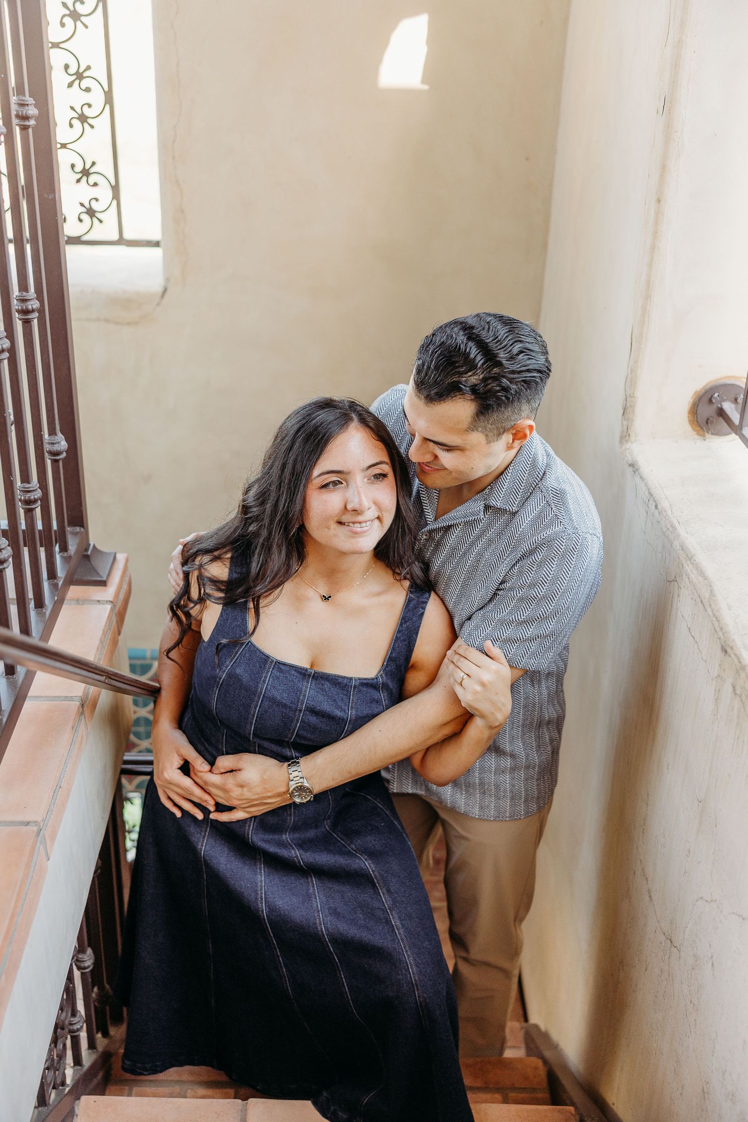 Couple embracing on vintage stairs with natural light streaming through window.
