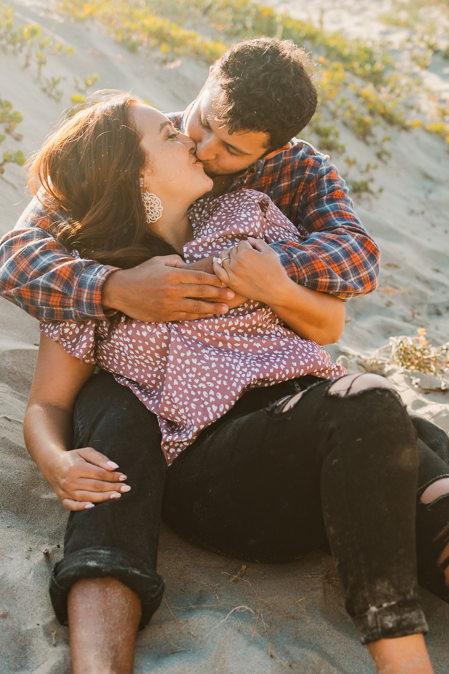 Romantic couple embracing on sandy beach during sunset photoshoot.