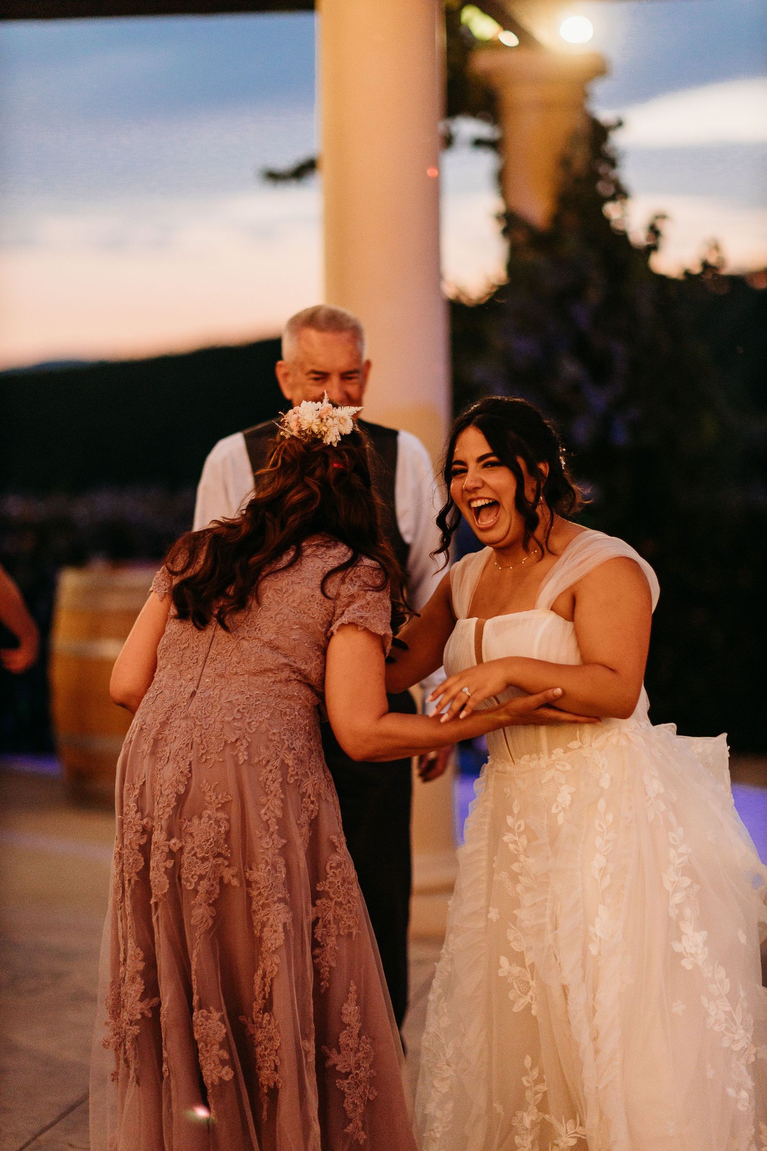 Wedding guests share a joyful moment laughing together at an outdoor evening reception.