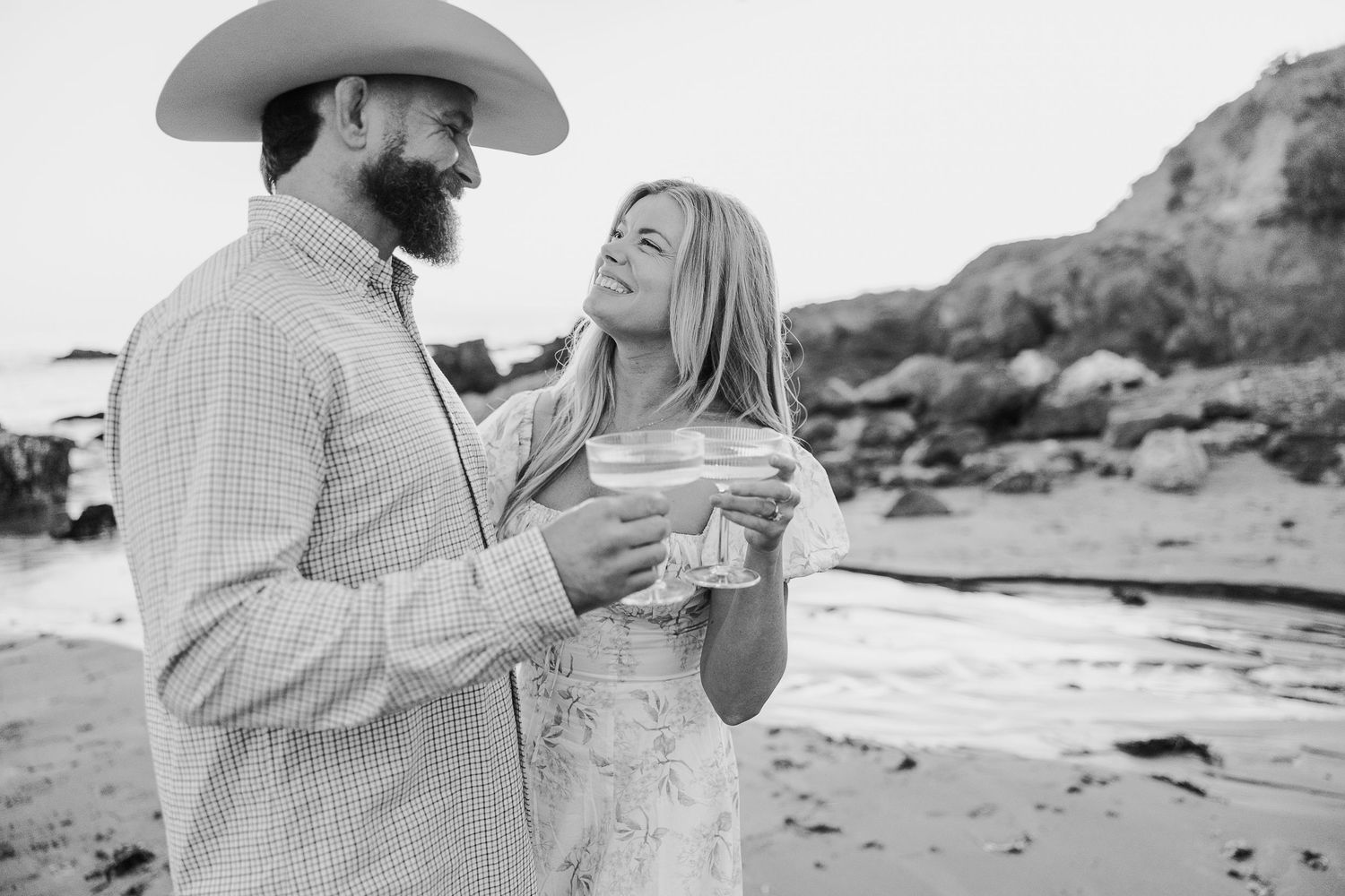 Couple toasting with champagne during sunset beach engagement session.