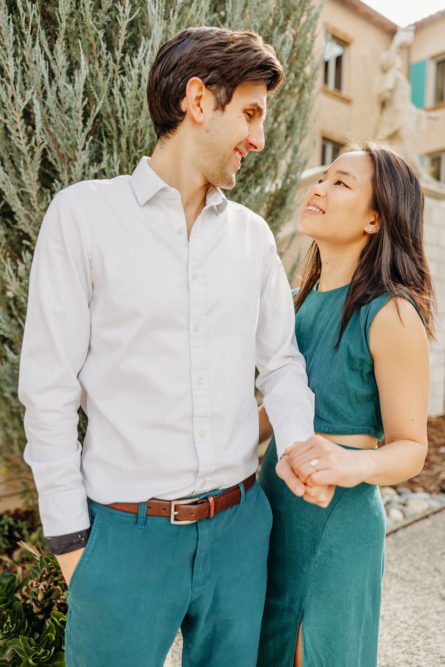 Romantic couple in coordinating green and white outfits share a tender moment outdoors against garden foliage.