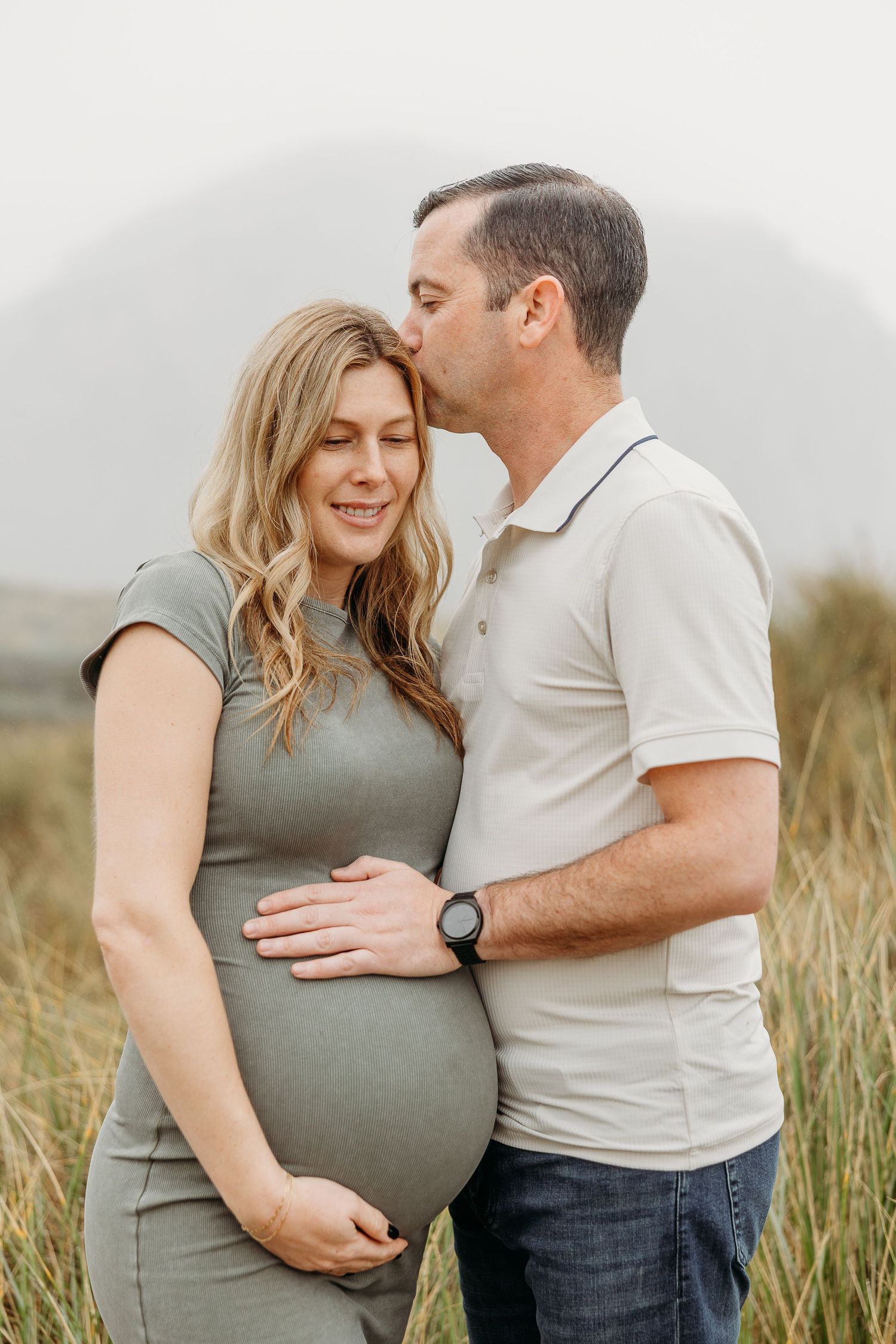 Intimate pregnancy portrait with tender kiss in natural outdoor setting.