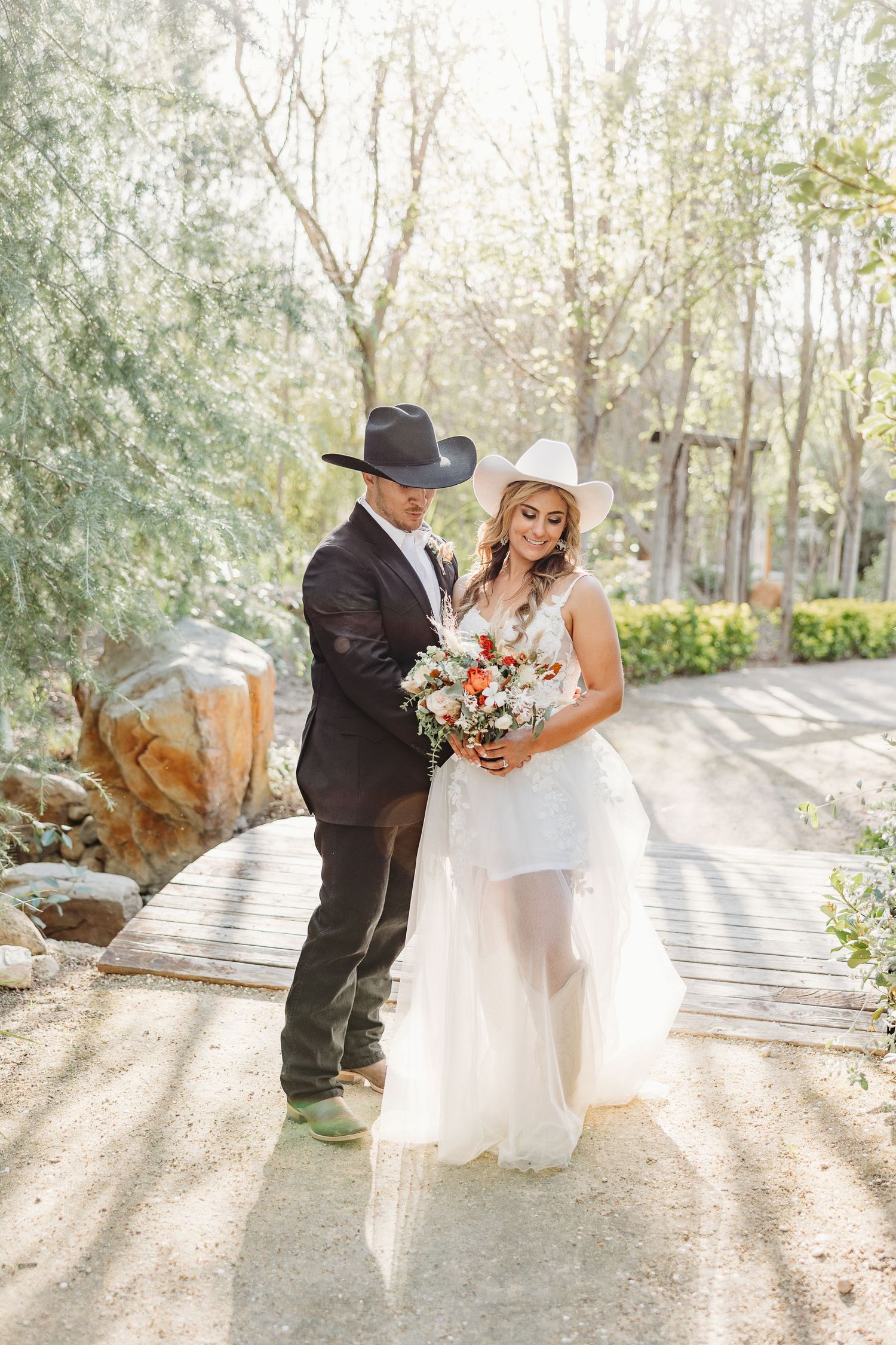 A couple in wedding attire shares a tender moment together on a sunlit garden path.