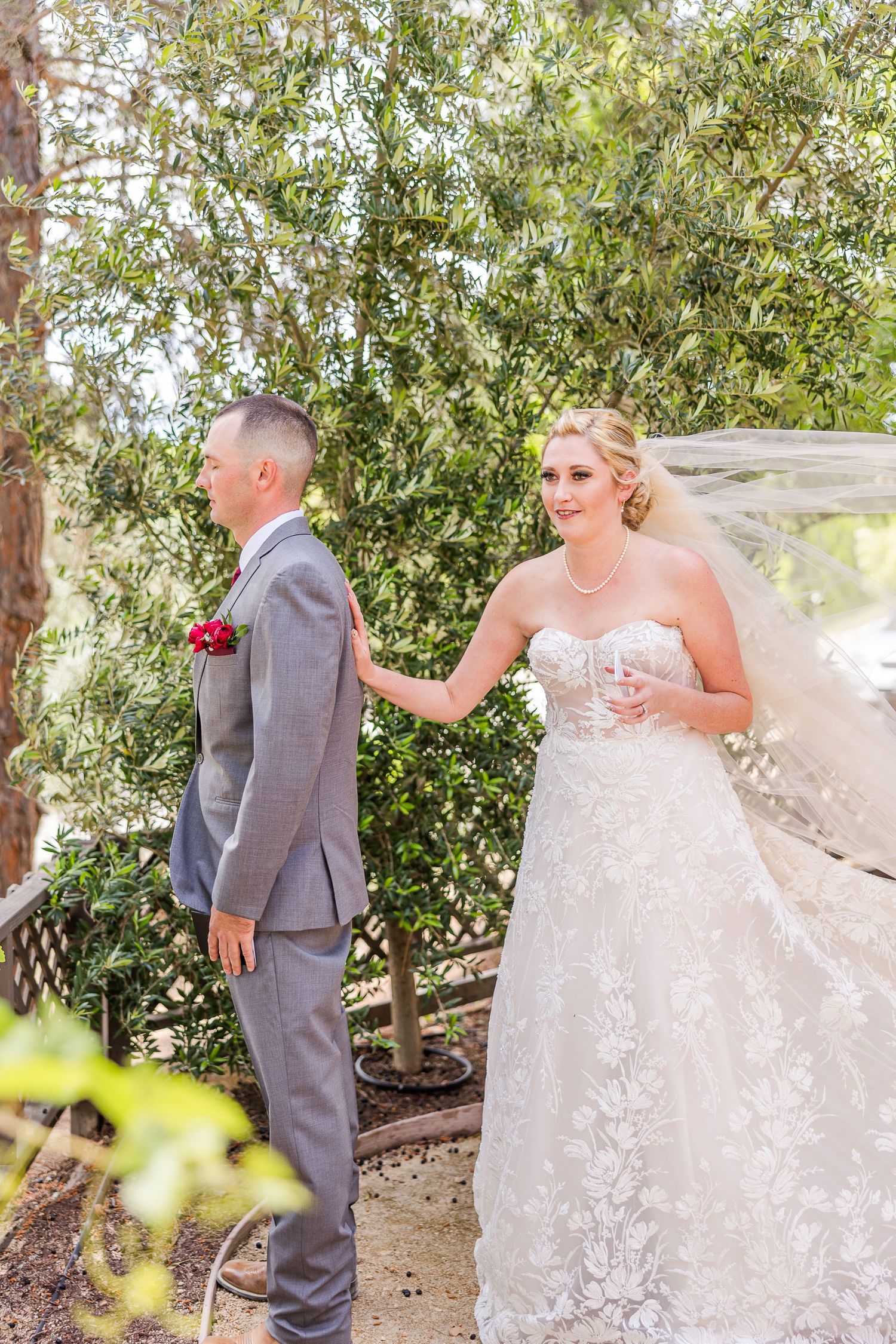 First look wedding moment in garden setting with bride in lace gown and groom in grey suit.
